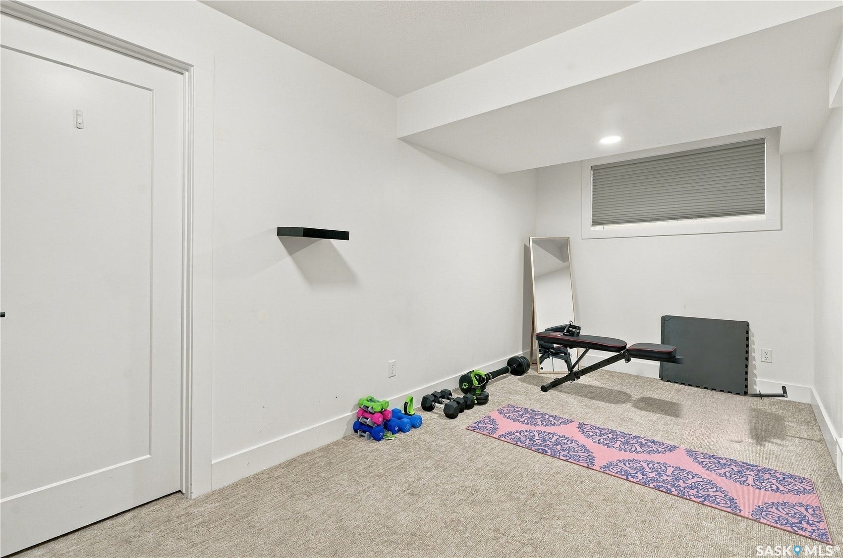 Recessed lighting, wall-mounted floating shelf, window with privacy blinds, white trim, and light-toned carpeting
