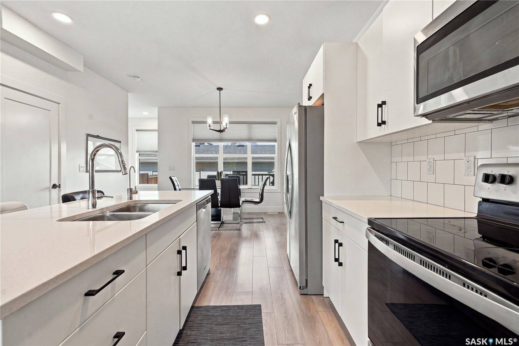 Kitchen featuring white cabinetry, stainless steel appliances, a subway tile backsplash, and a large island with a double basin sink