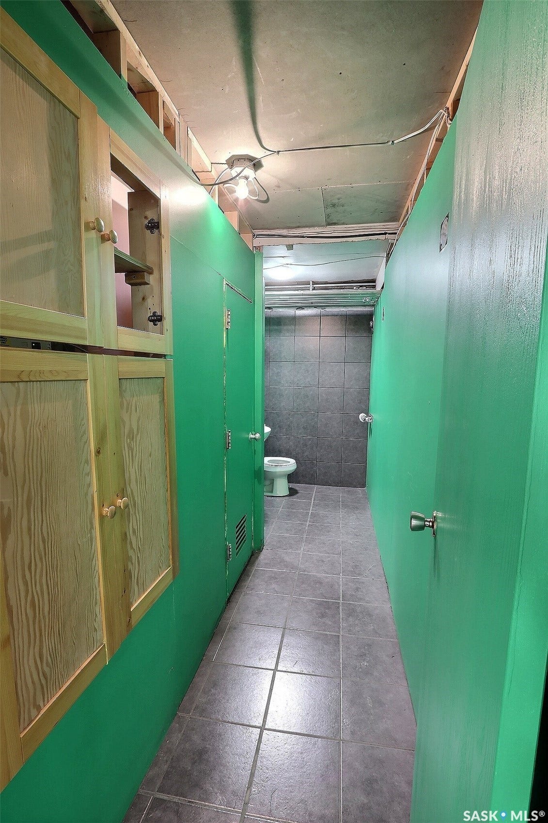 Tiled flooring with a toilet and green wall partitions, featuring a built-in wooden cabinet