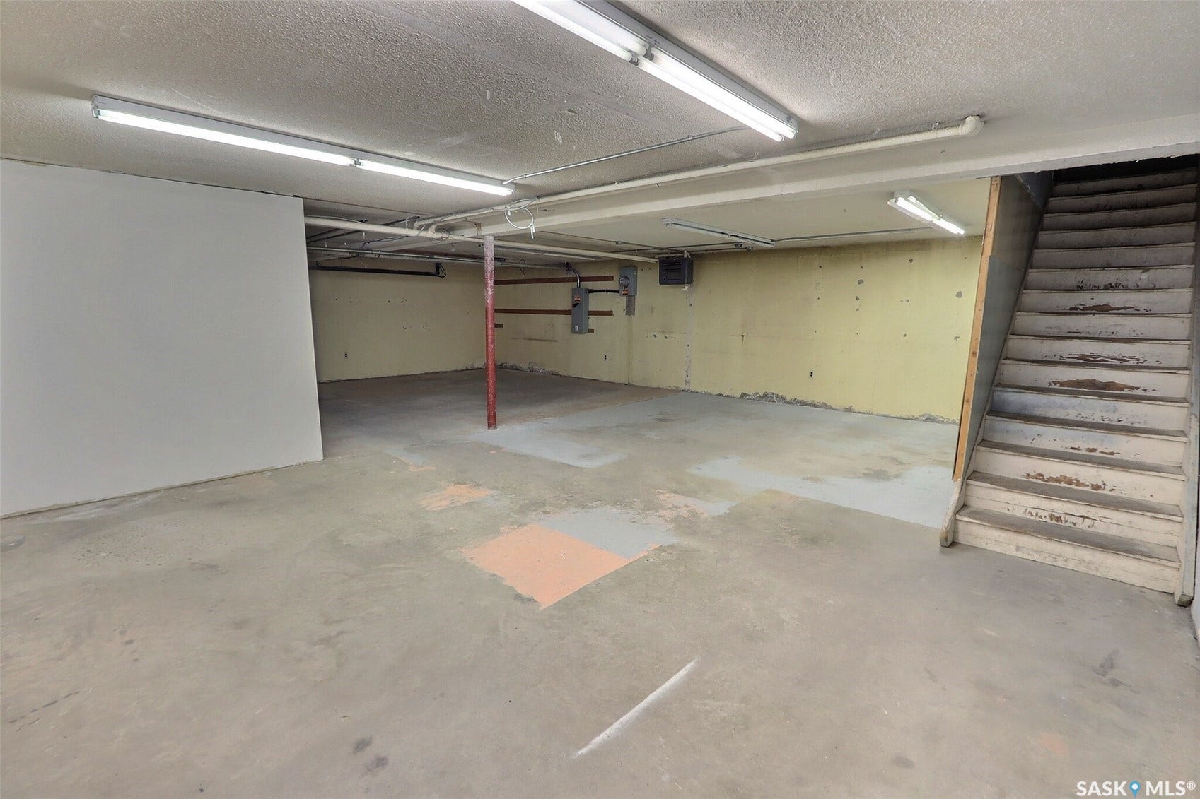 Concrete flooring with exposed ceiling utilities, fluorescent lighting, and a partial wall partition