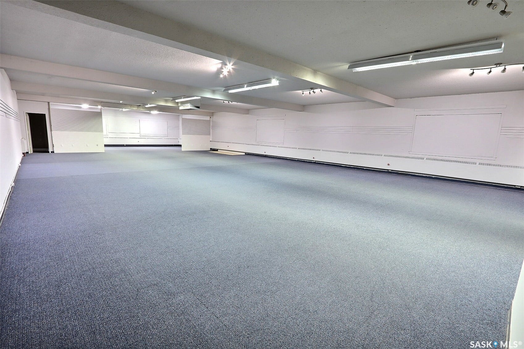 Spacious commercial or multi-use interior featuring pristine carpeted flooring, recessed and track lighting throughout, and white painted walls with extensive whiteboard surfaces