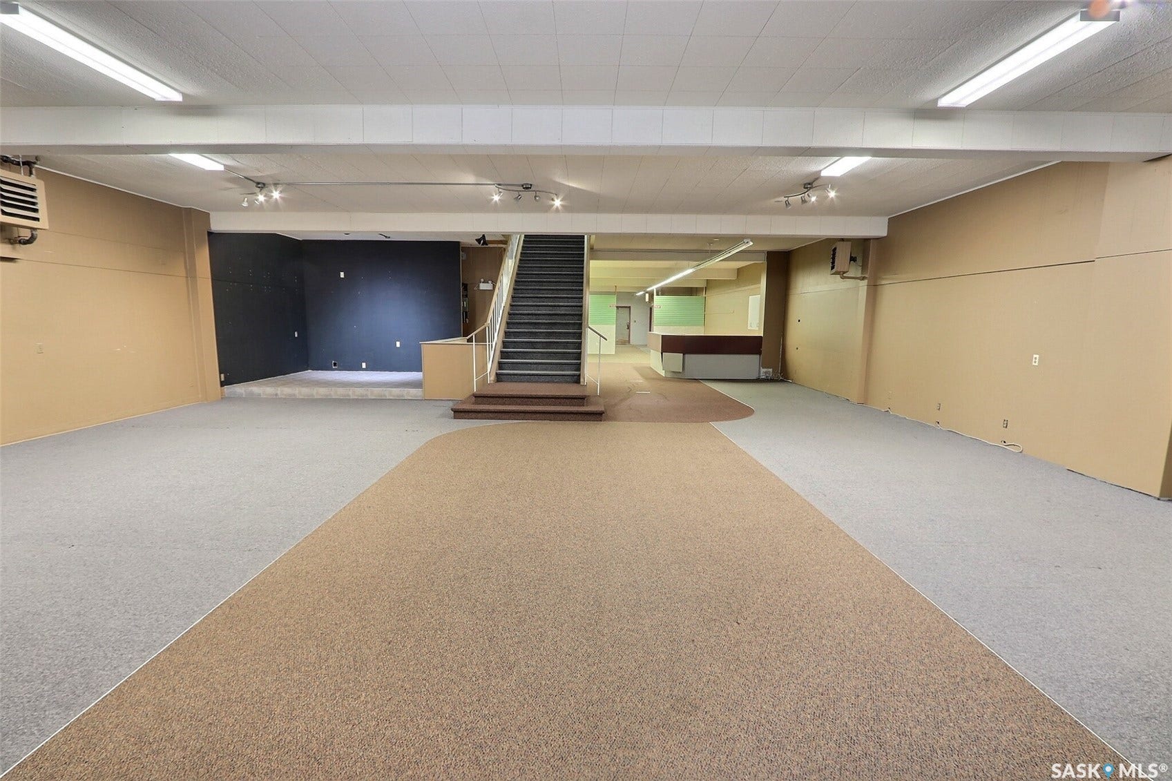 Expansive open-plan area featuring mixed-tone carpeting, a built-in staircase with dark treads, and a built-in counter