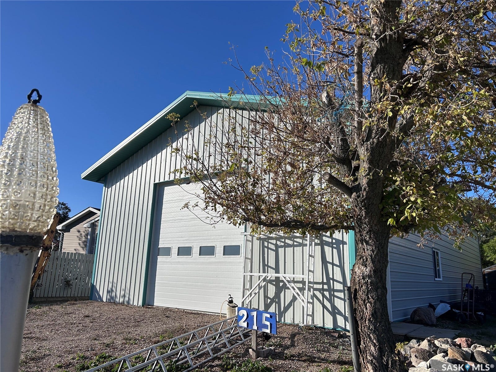 207 1st Street, North Portal SK S0C 1W0 Metal-sided outbuilding with a green metal roof, featuring a large white garage door with horizontal window inserts