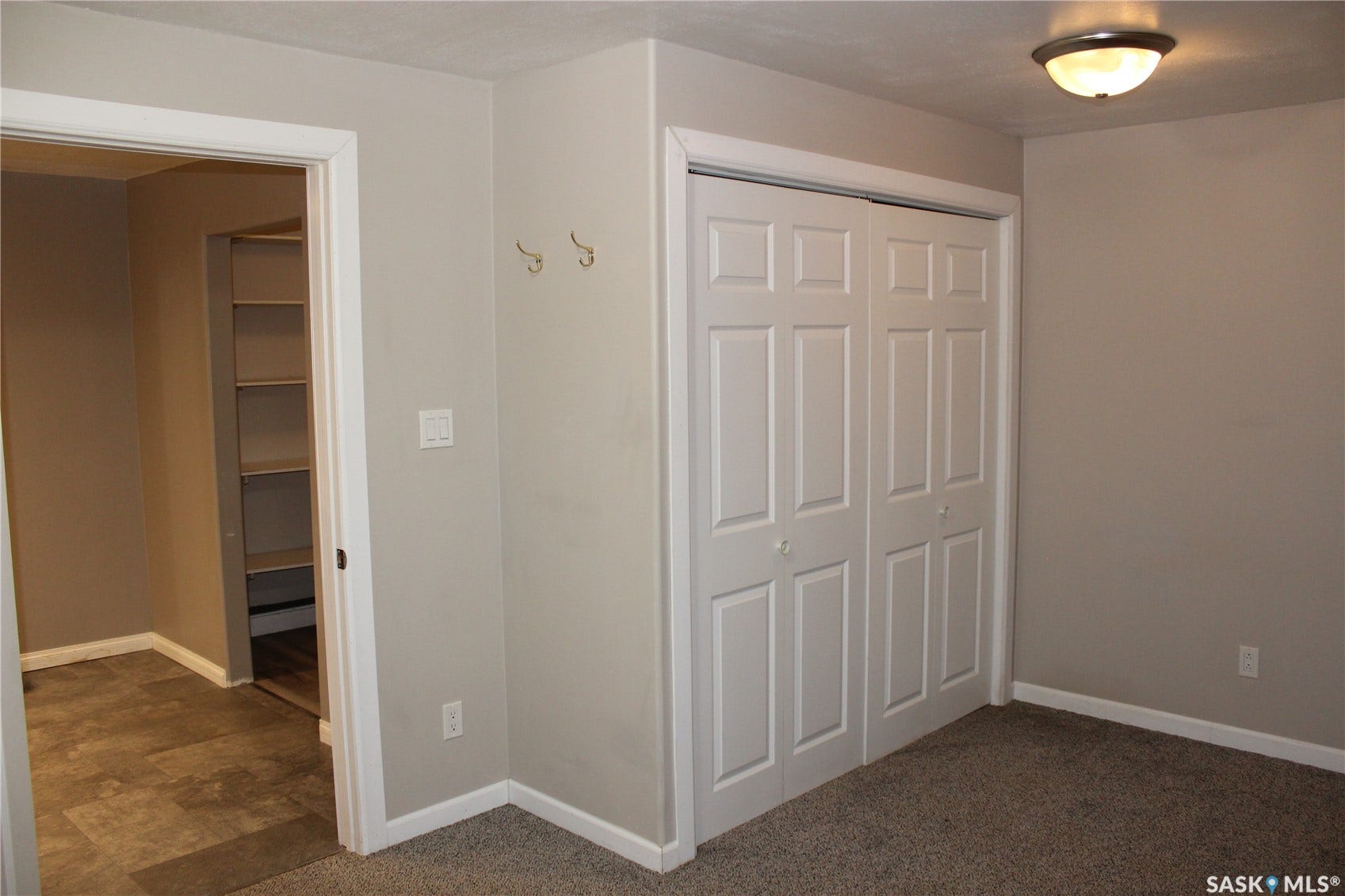 Carpeted flooring, bi-fold panel doors, brass wall hooks, built-in shelving, and a semi-flush mount ceiling light fixture