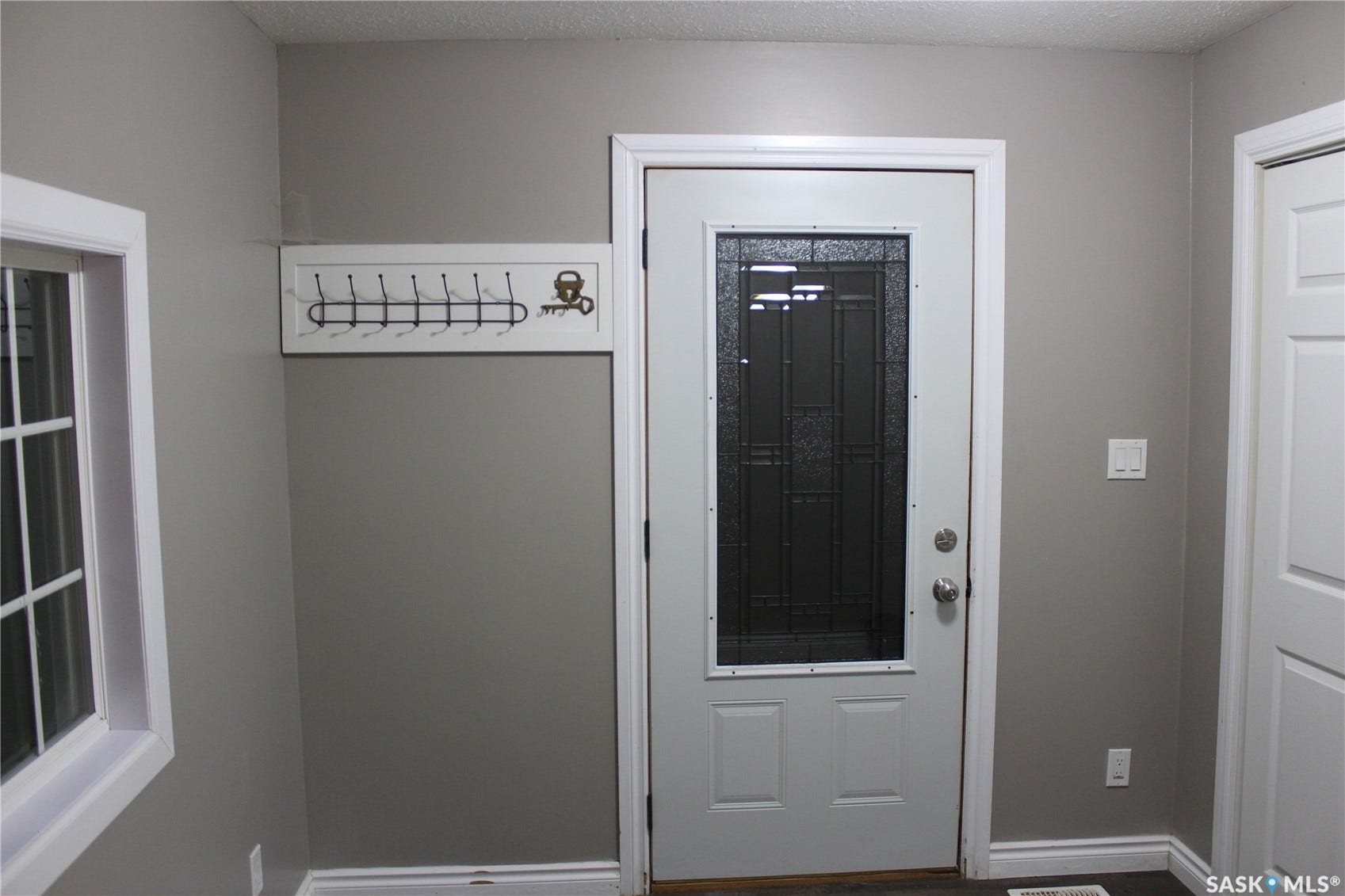 Entry with a white door featuring a decorative glass insert, complemented by a white-trimmed window, neutral wall paint, and dark flooring