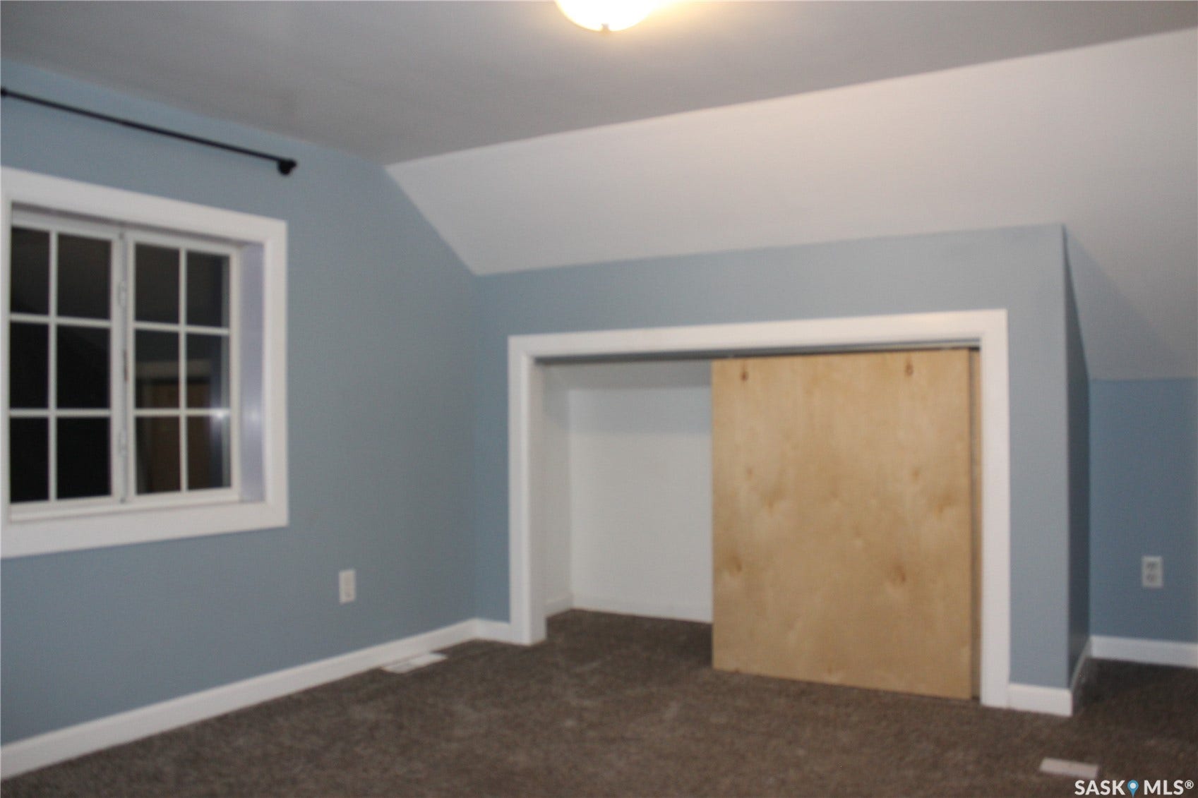 Vaulted ceiling, window with white trim, light blue wall paint, barn door style closet door, and carpeted flooring