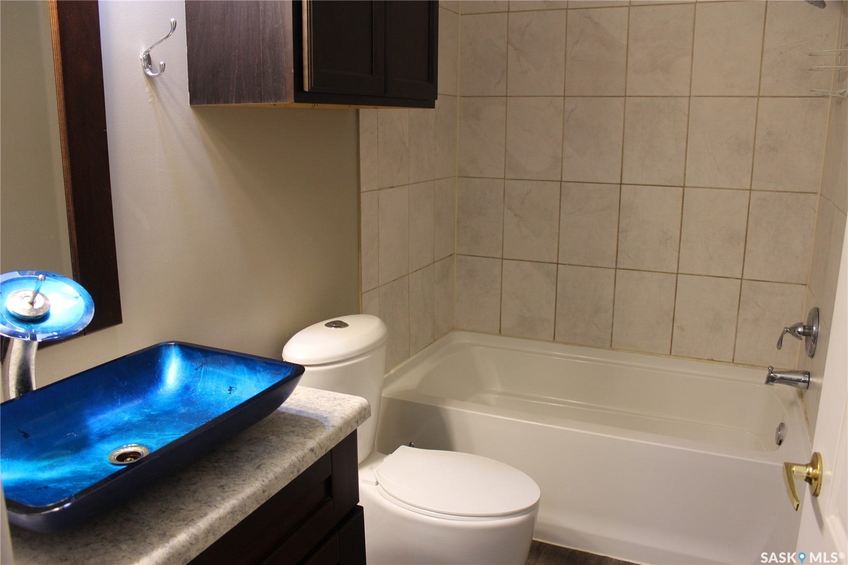 Bathroom featuring a vessel sink with a unique blue finish, a dark wood-finish vanity, a white bathtub, and tiled shower surround