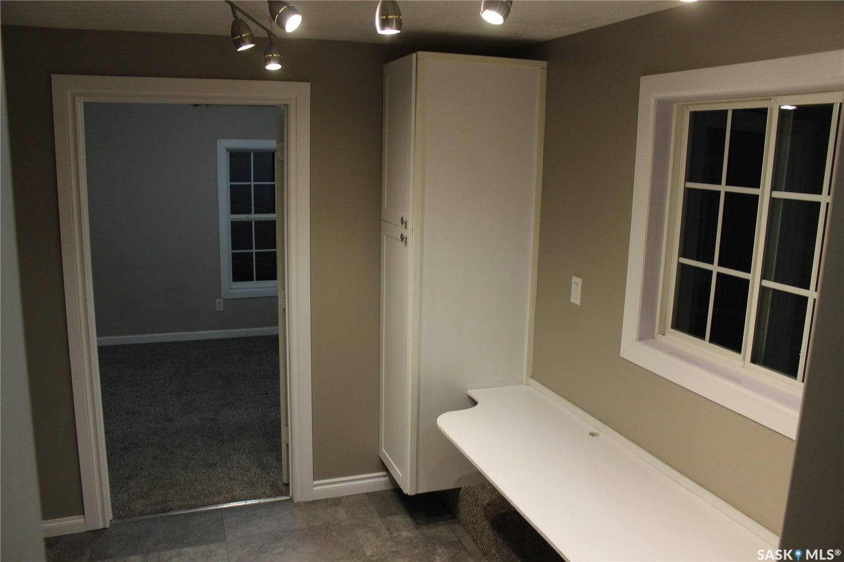 Built-in desk with overhead track lighting, adjacent built-in cabinetry, and a window with grilles