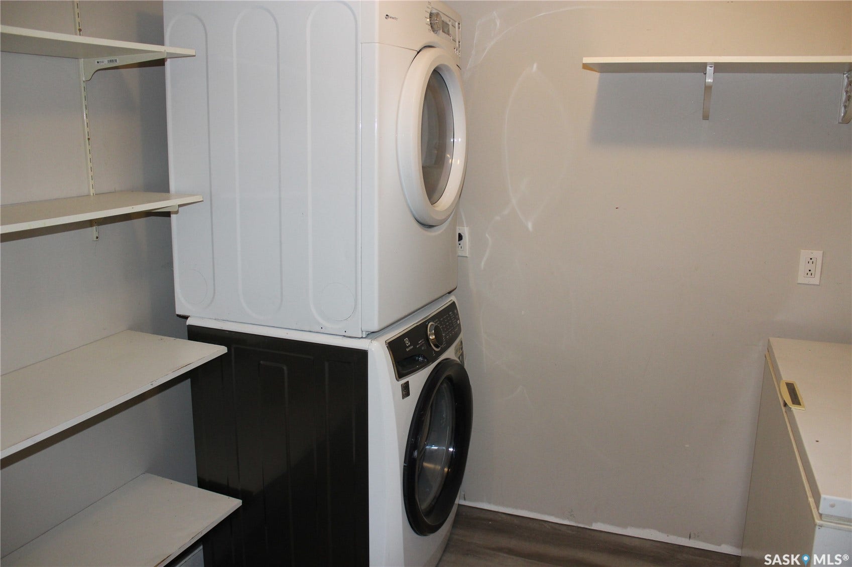Laundry area with stacked appliances, open shelving, and light-toned flooring