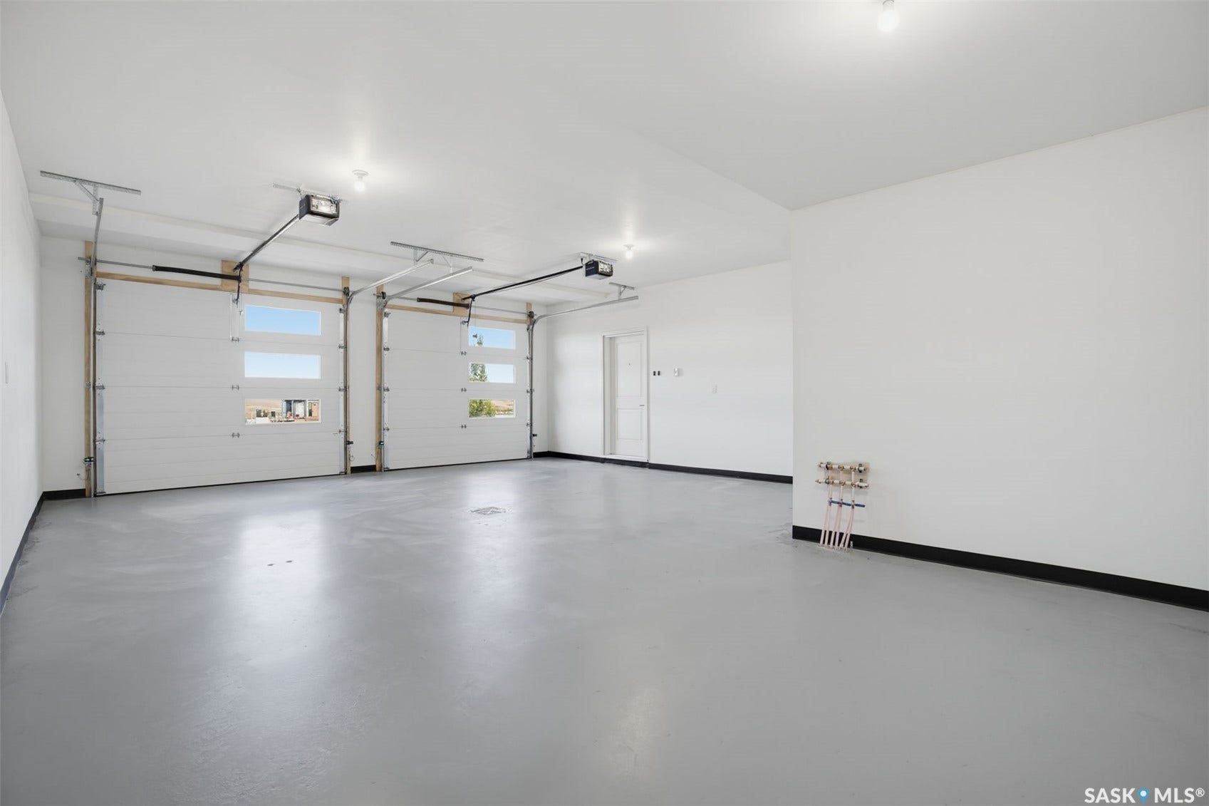 Spacious garage featuring two overhead doors with window panels, a smooth concrete floor, and white painted walls