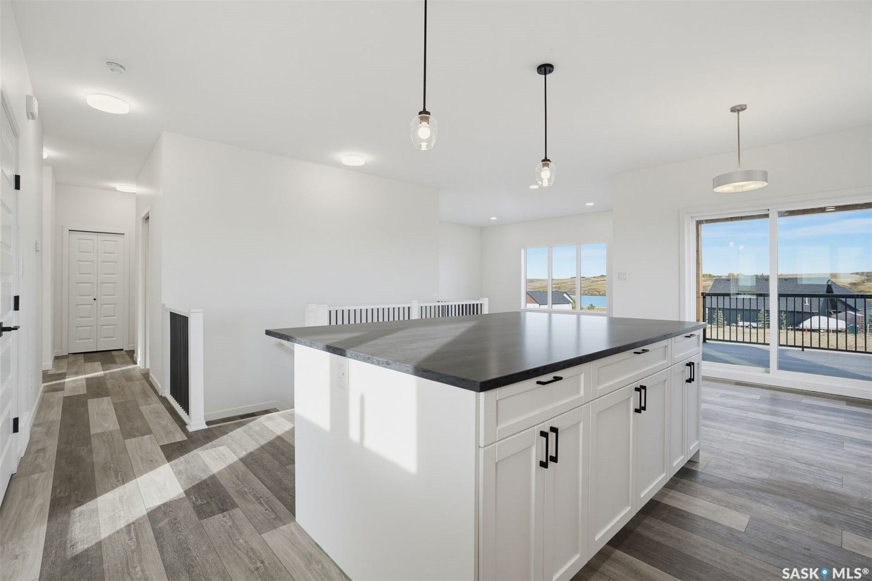 Kitchen island with a dark countertop and white cabinetry, wood-finish flooring, and a sliding glass door providing access to an exterior deck