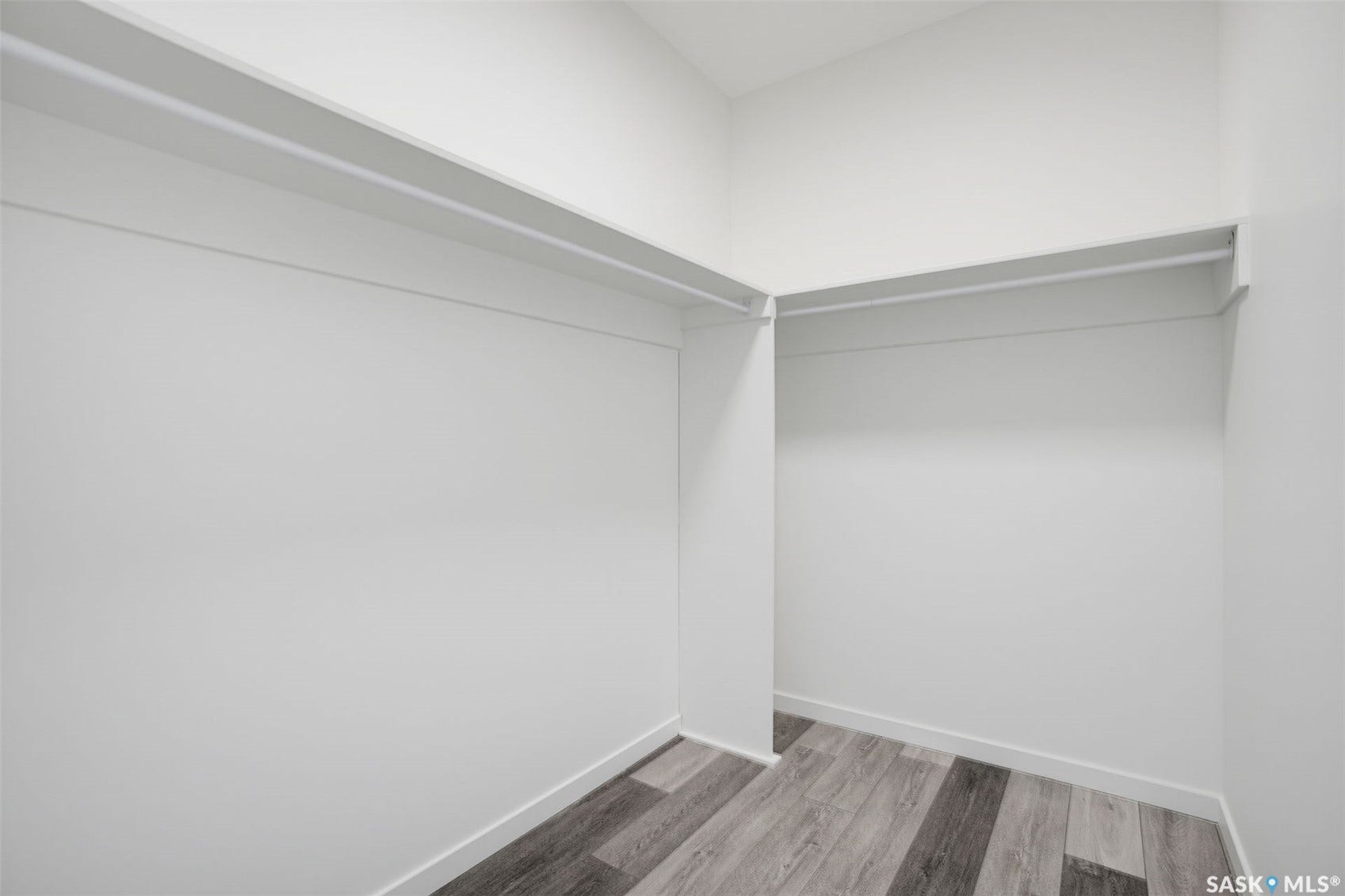 Walk-in closet featuring white walls, white shelving, white hanging rods, and wood-finish flooring