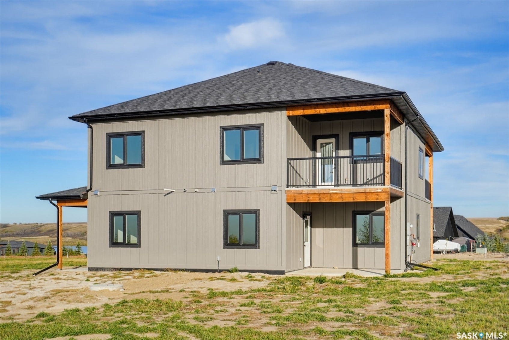 Two-story structure with gray siding, black-framed windows, a black asphalt shingle roof, and a covered balcony featuring a black metal railing and wood-finish supports