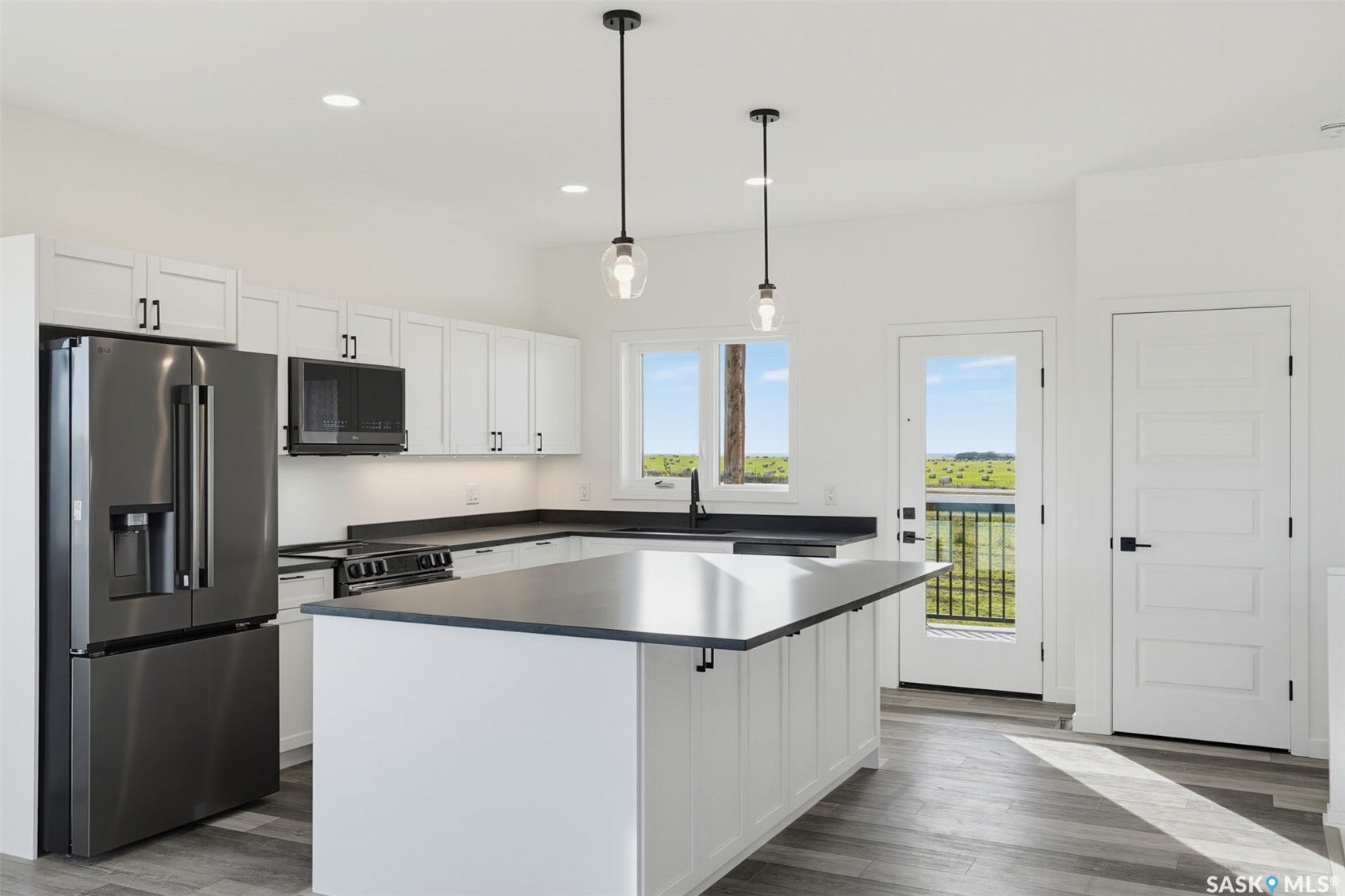 Modern kitchen featuring stainless steel appliances, crisp white cabinetry with black hardware, dark countertops, and wood-finish flooring