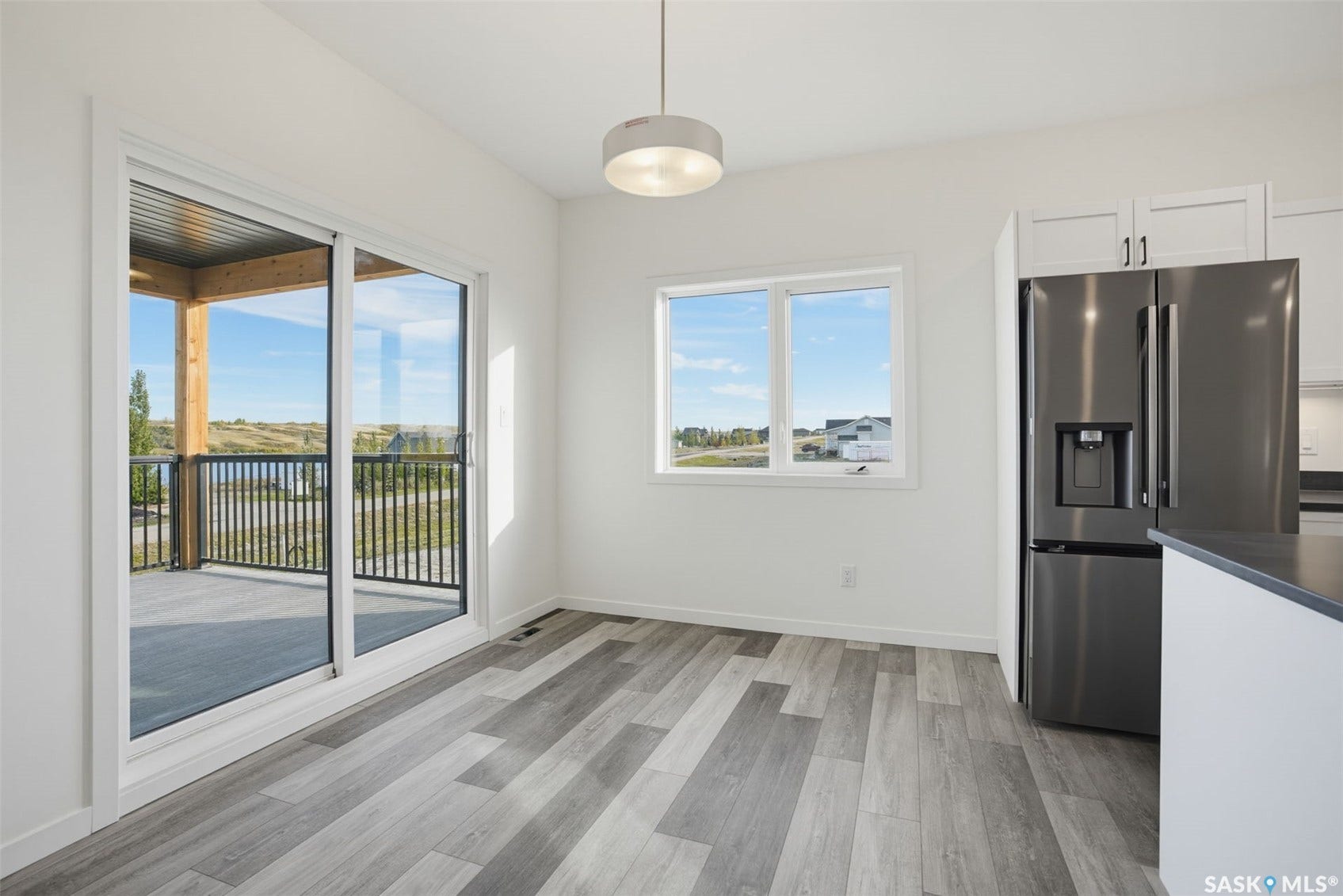 Sliding glass doors leading to a covered balcony with black metal railing, grey wood-finish flooring, white walls, and a stainless steel refrigerator