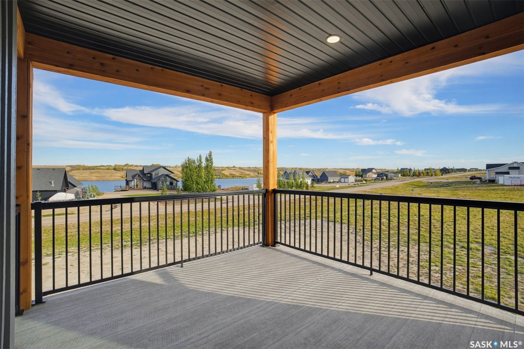 Covered deck with a textured concrete surface, black metal railings, and a wood-beamed ceiling featuring recessed lighting