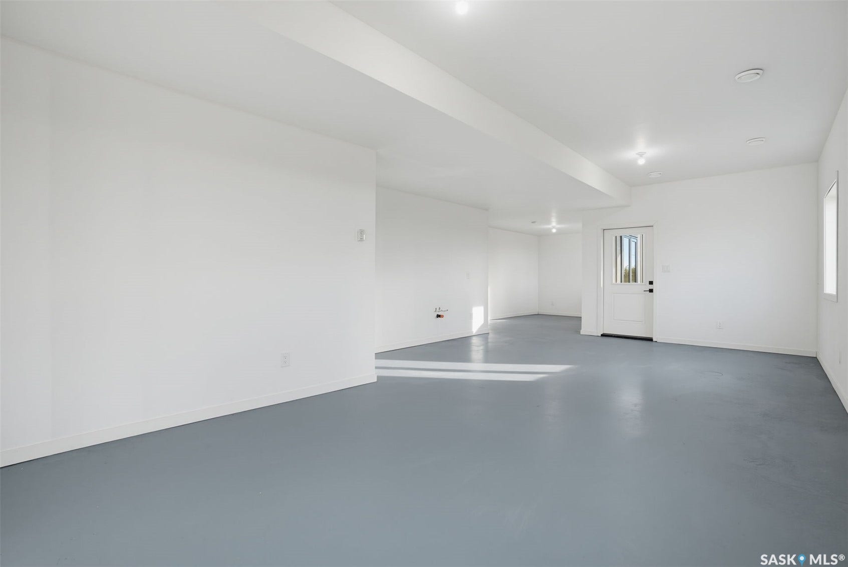 Spacious room with painted concrete flooring, recessed lighting, and a white paneled door