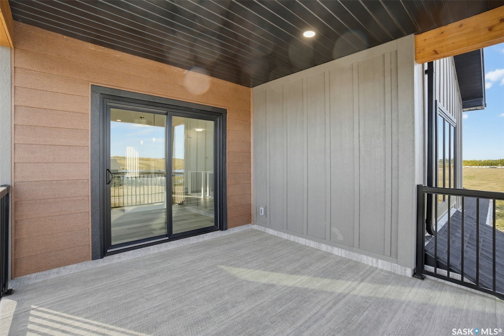 Exterior balcony with textured concrete flooring, black metal railing, and a sliding glass door