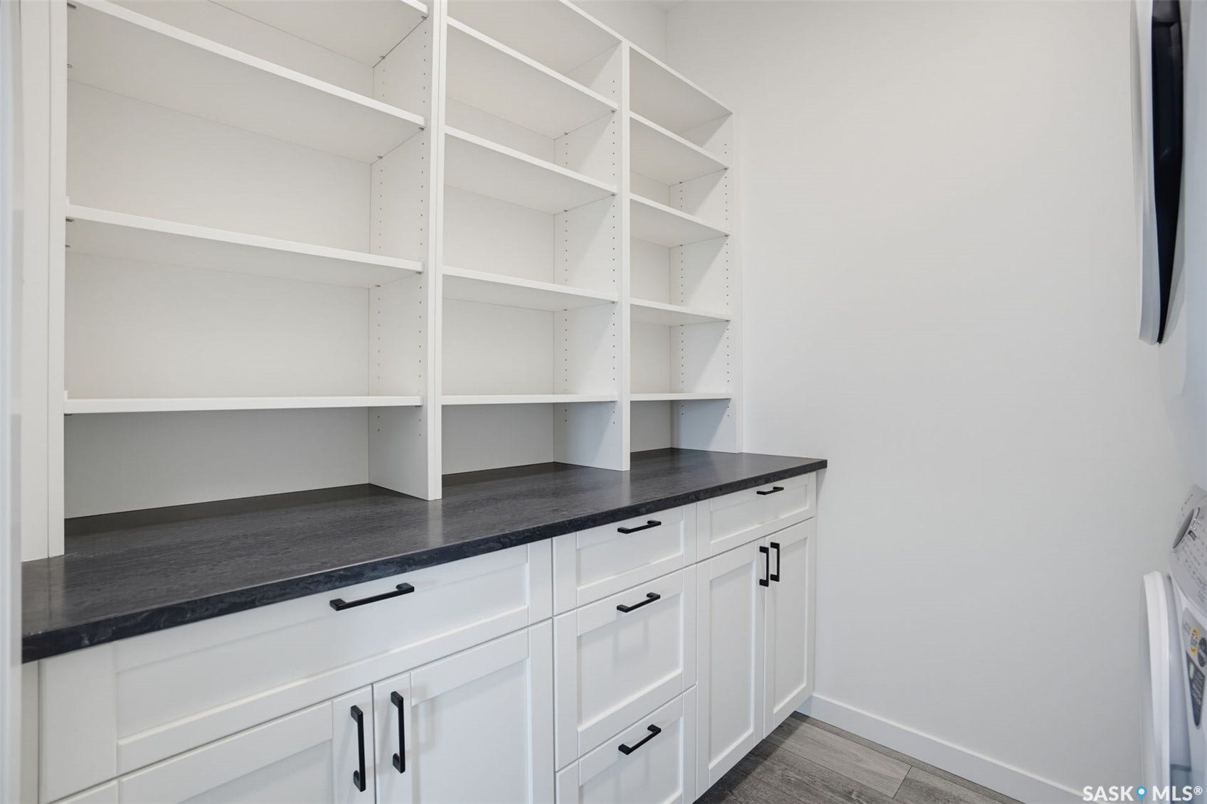White built-in shelving, white cabinetry with matte black hardware, and a dark countertop