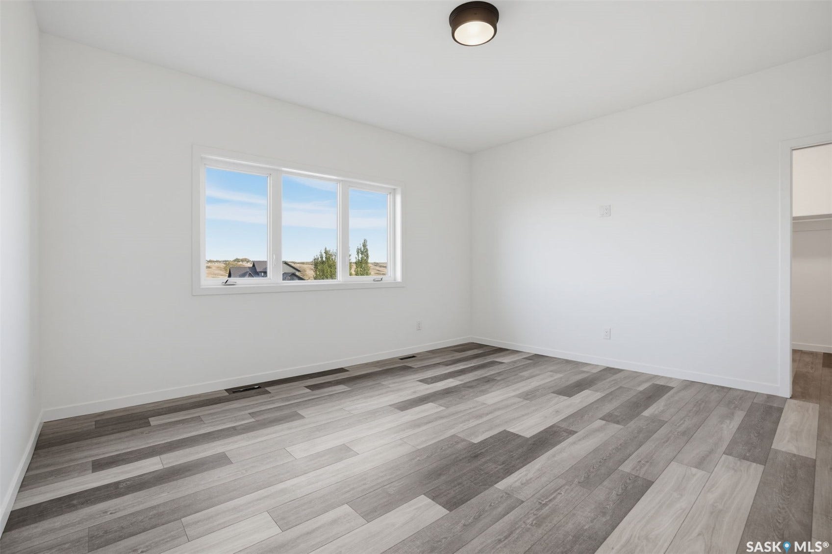 White interior walls with multi-pane window, wood-finish plank flooring, and a flush mount ceiling light fixture