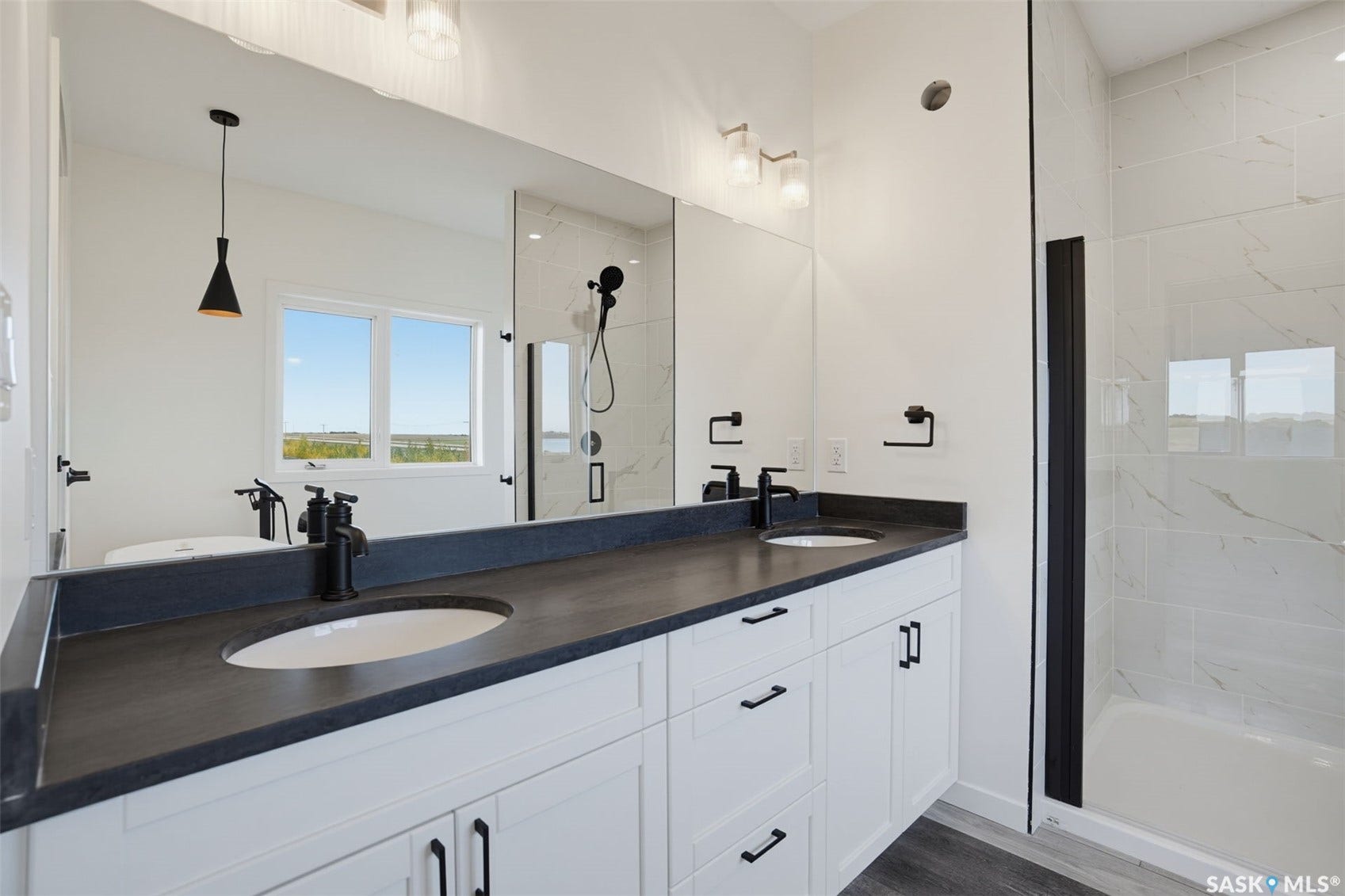 Dual vanity with dark countertops, white cabinetry, matte black hardware, and an adjacent shower with a clear glass enclosure