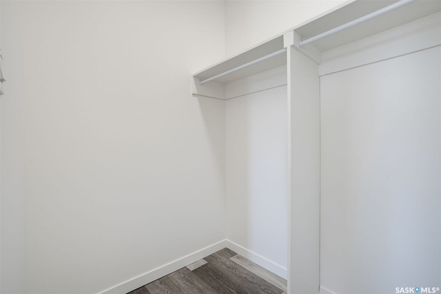 Walk-in closet with white shelving, hanging rods, and wood-finish flooring