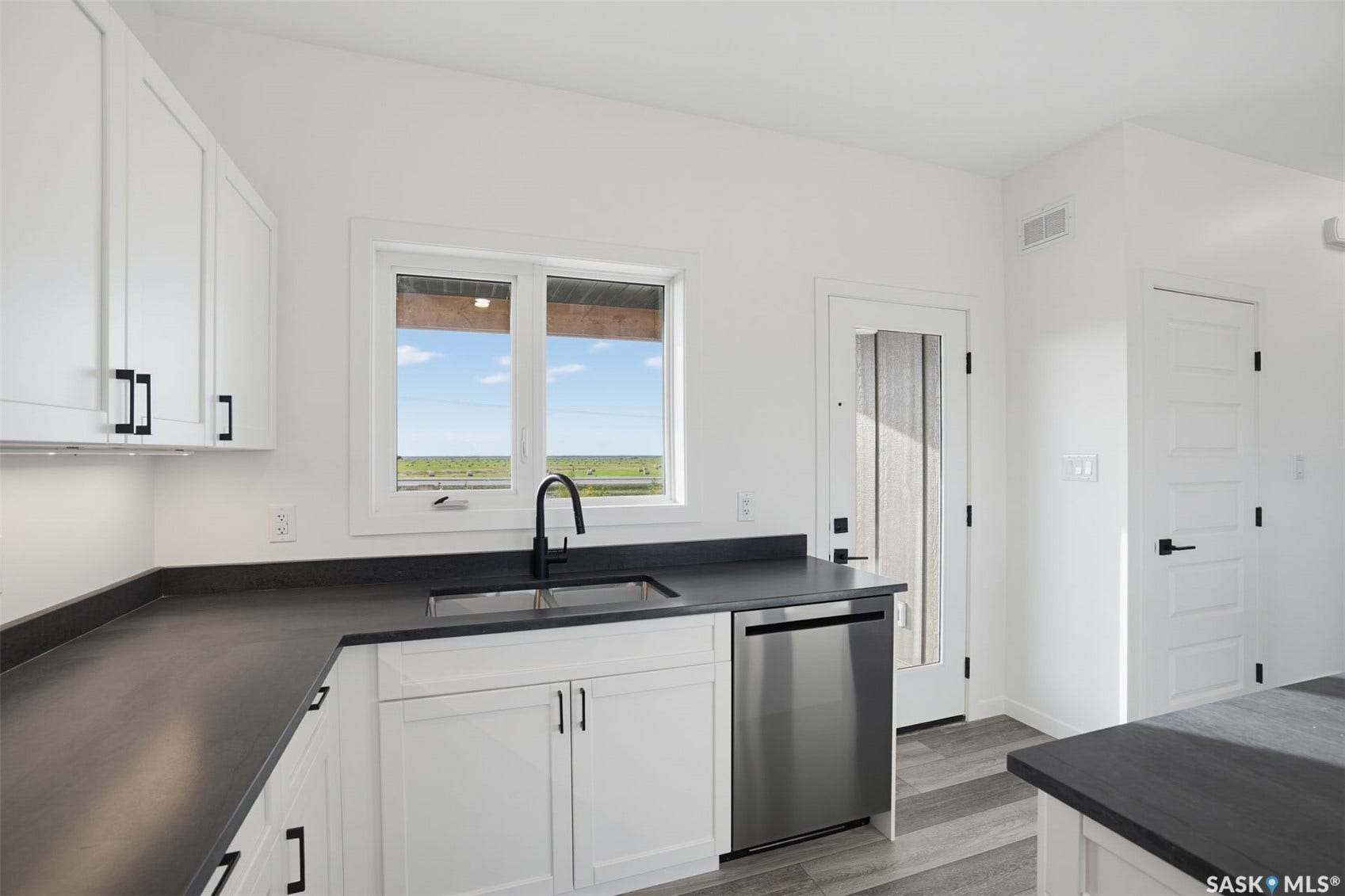 Modern kitchen featuring white cabinetry, dark countertops, a stainless steel dishwasher, and a black gooseneck faucet