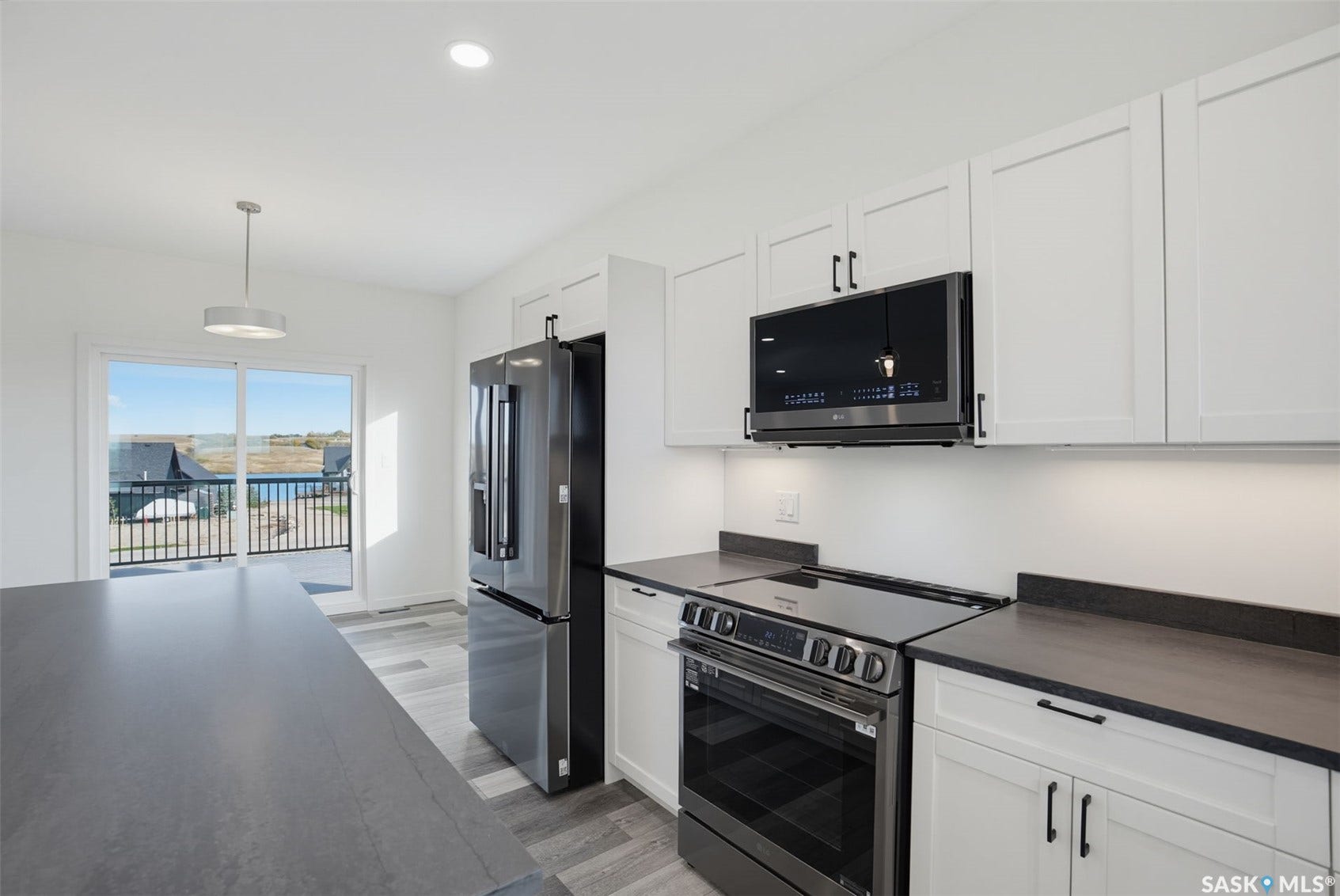 White shaker cabinetry with dark hardware, stainless steel appliances, dark countertops, and wood-finish flooring