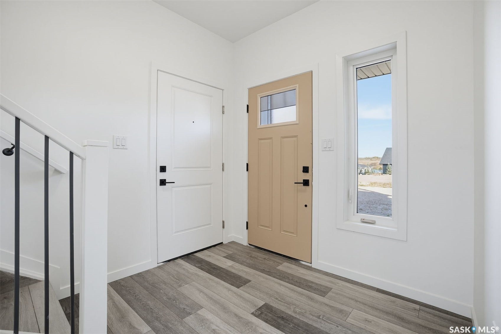 Entryway featuring wood-finish flooring, a white paneled door, a beige door with an upper glass panel, and a vertical window