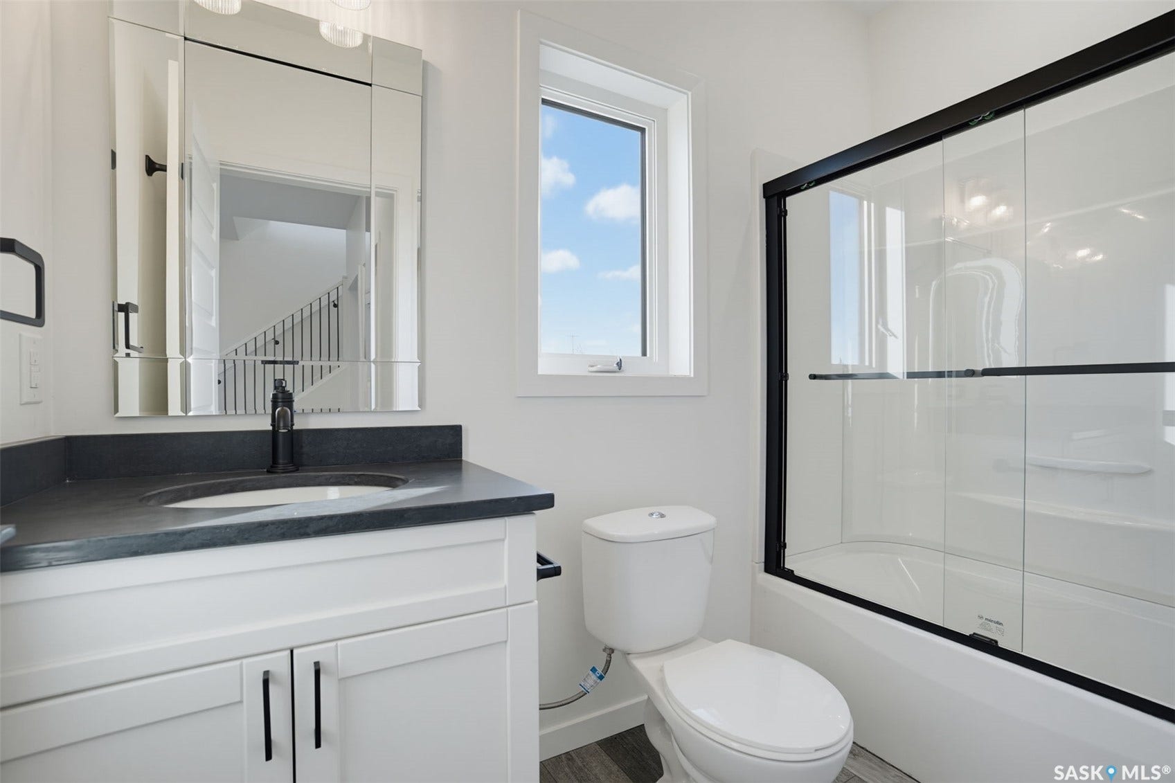 Bathroom featuring a white vanity with dark countertop, undermount sink, black fixtures, and a shower-tub combination with black-framed glass doors