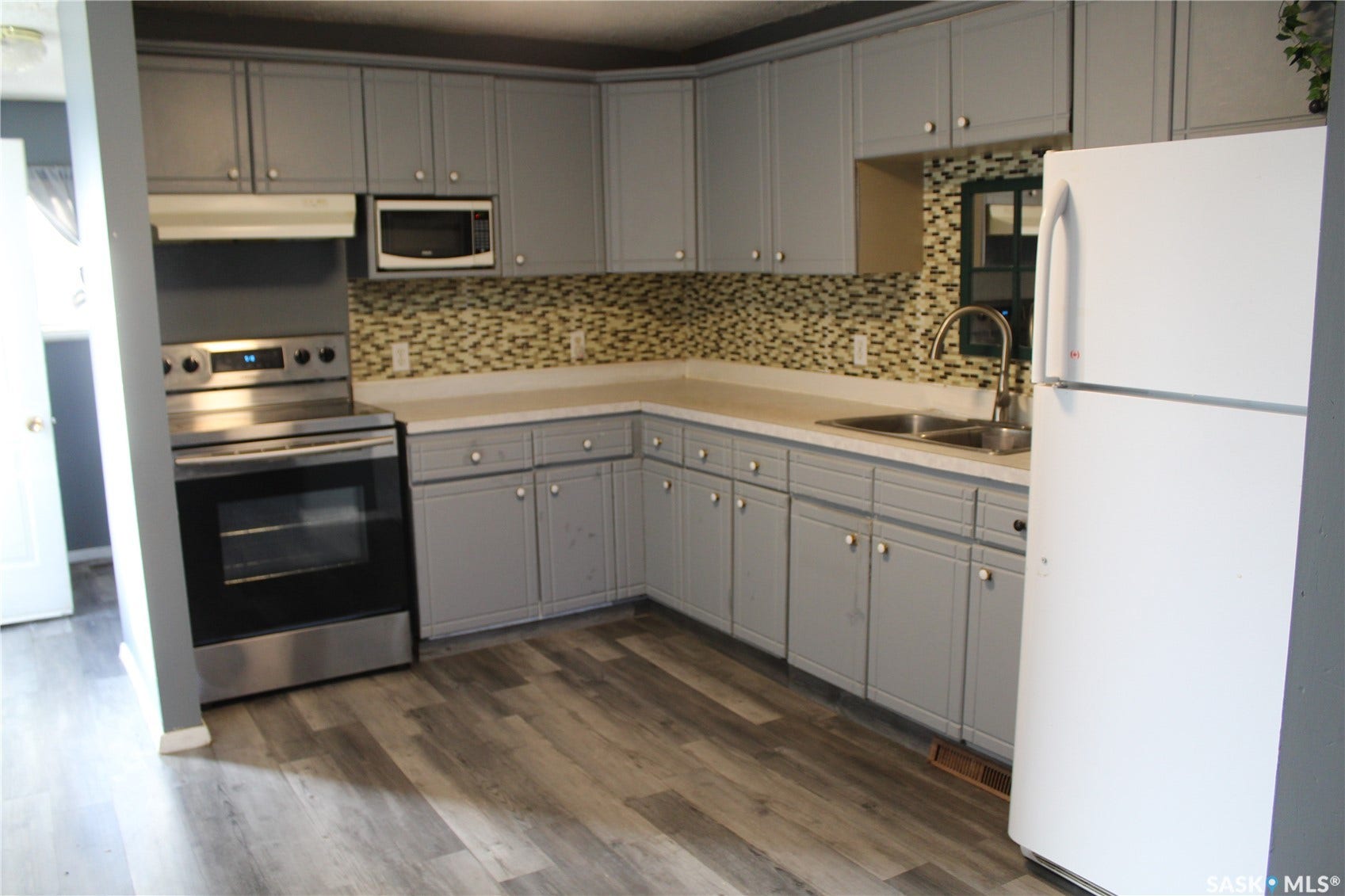 513 2nd Street W, Wilkie SK S0K 4W0 Light gray cabinetry, stainless steel range, built-in microwave, wood-finish flooring, and a mosaic tile backsplash