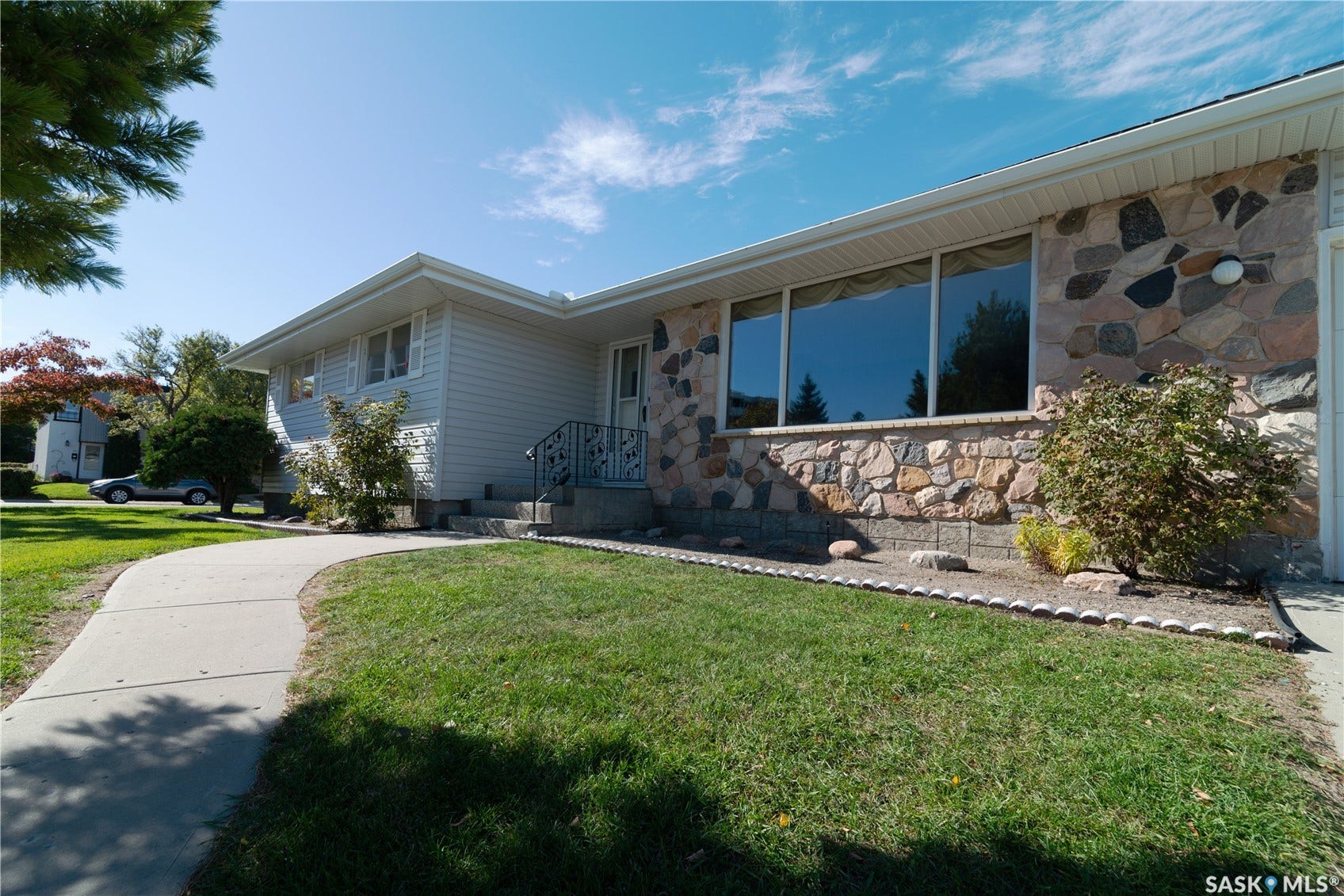 Stone veneer facade with large picture windows, white siding, and a concrete pathway