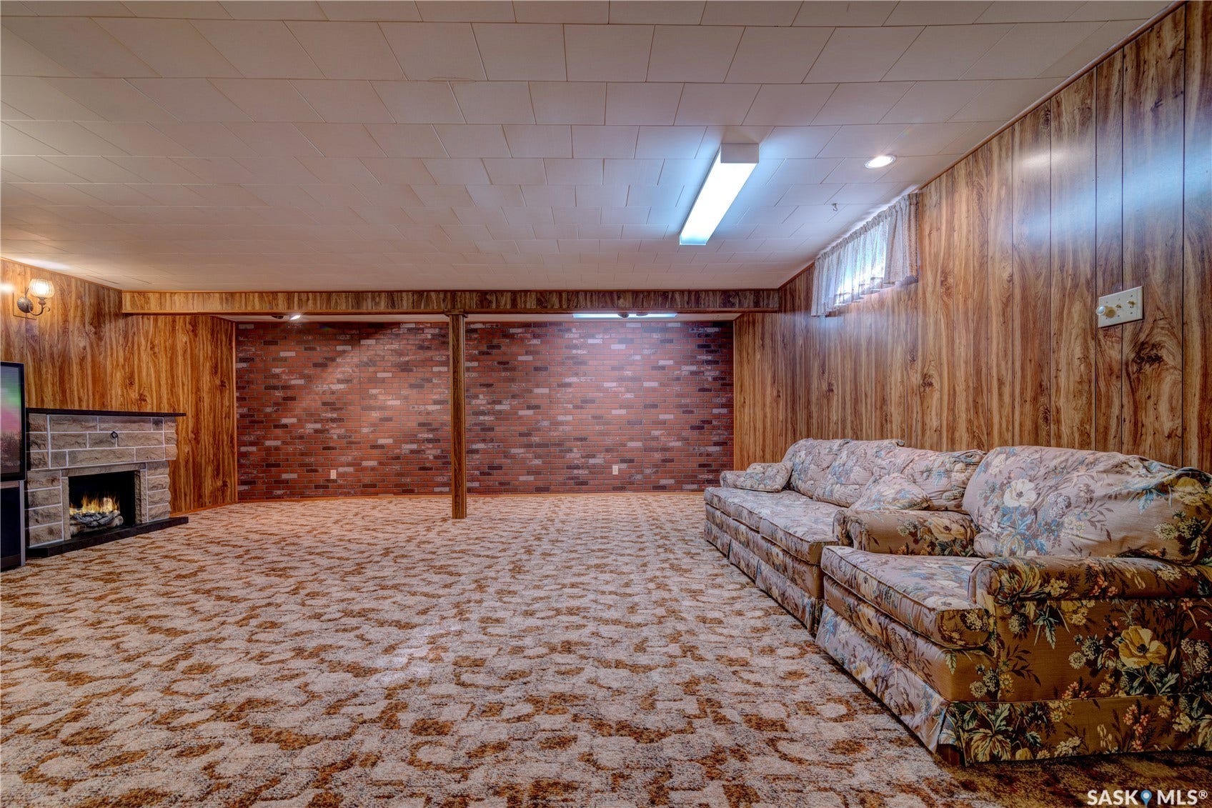 Spacious room featuring wood-finish wall panels and a brick accent wall