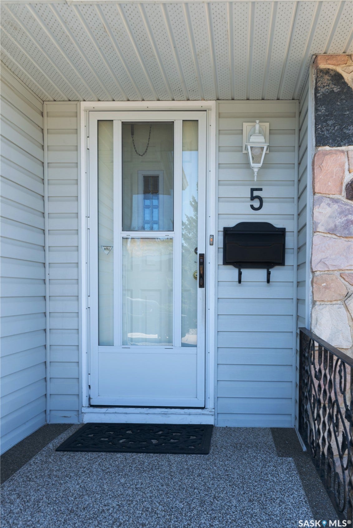 White siding exterior with stone accent column, black metal railing, and exposed aggregate concrete porch