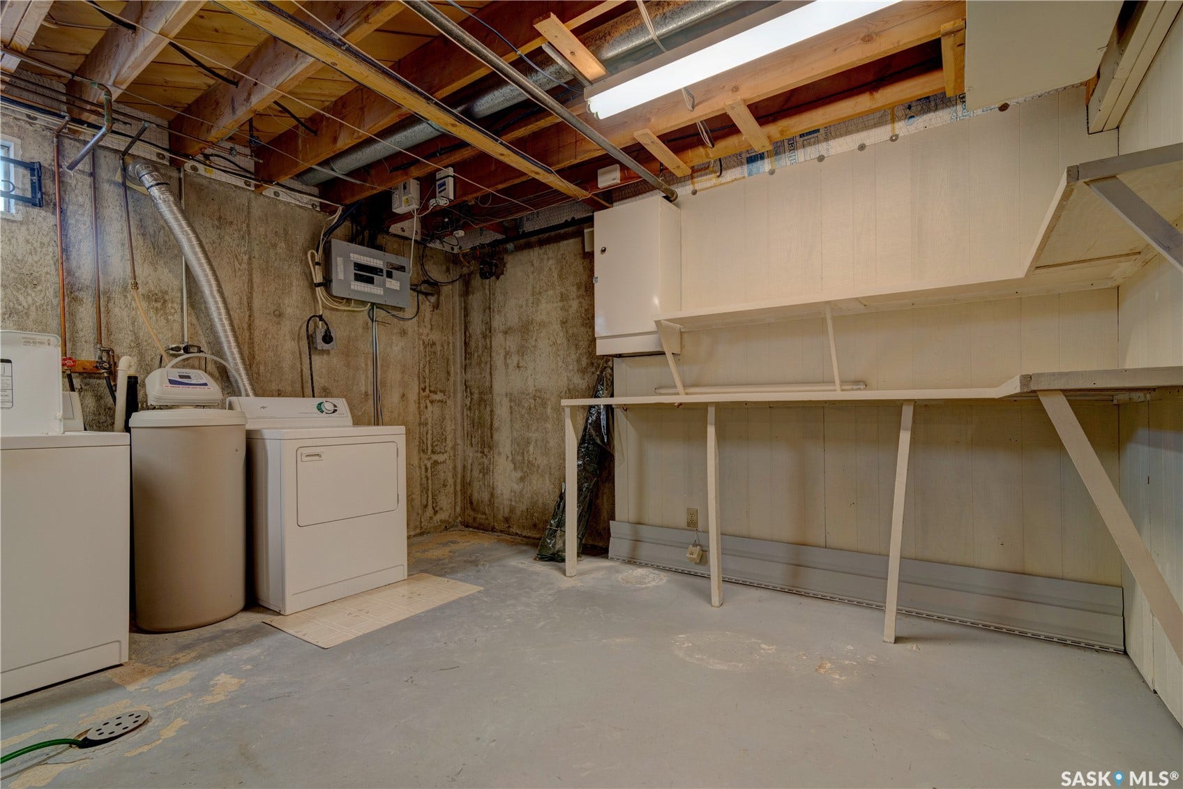Utility space featuring exposed ceiling joists, concrete foundation walls, a water treatment system, and built-in shelving
