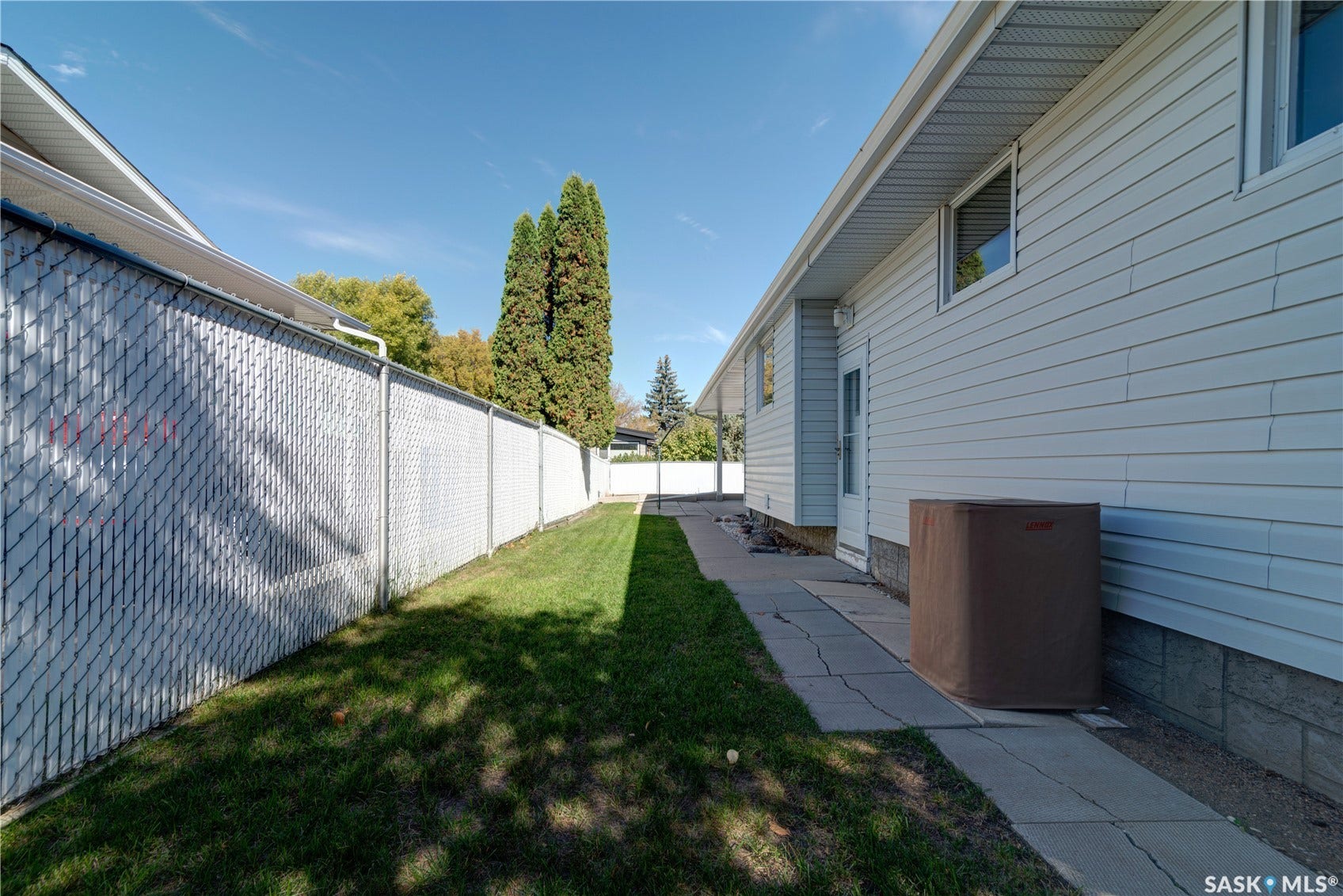 Side yard featuring a chain-link fence with privacy slats, concrete paver pathway, and a grassy area
