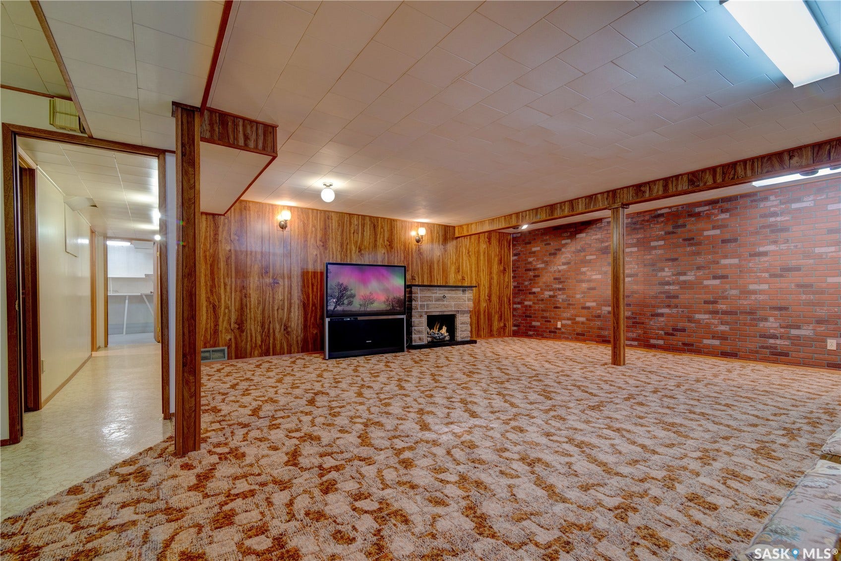 Finished lower level featuring a fireplace, brick wall accents, wood paneling, and drop ceiling