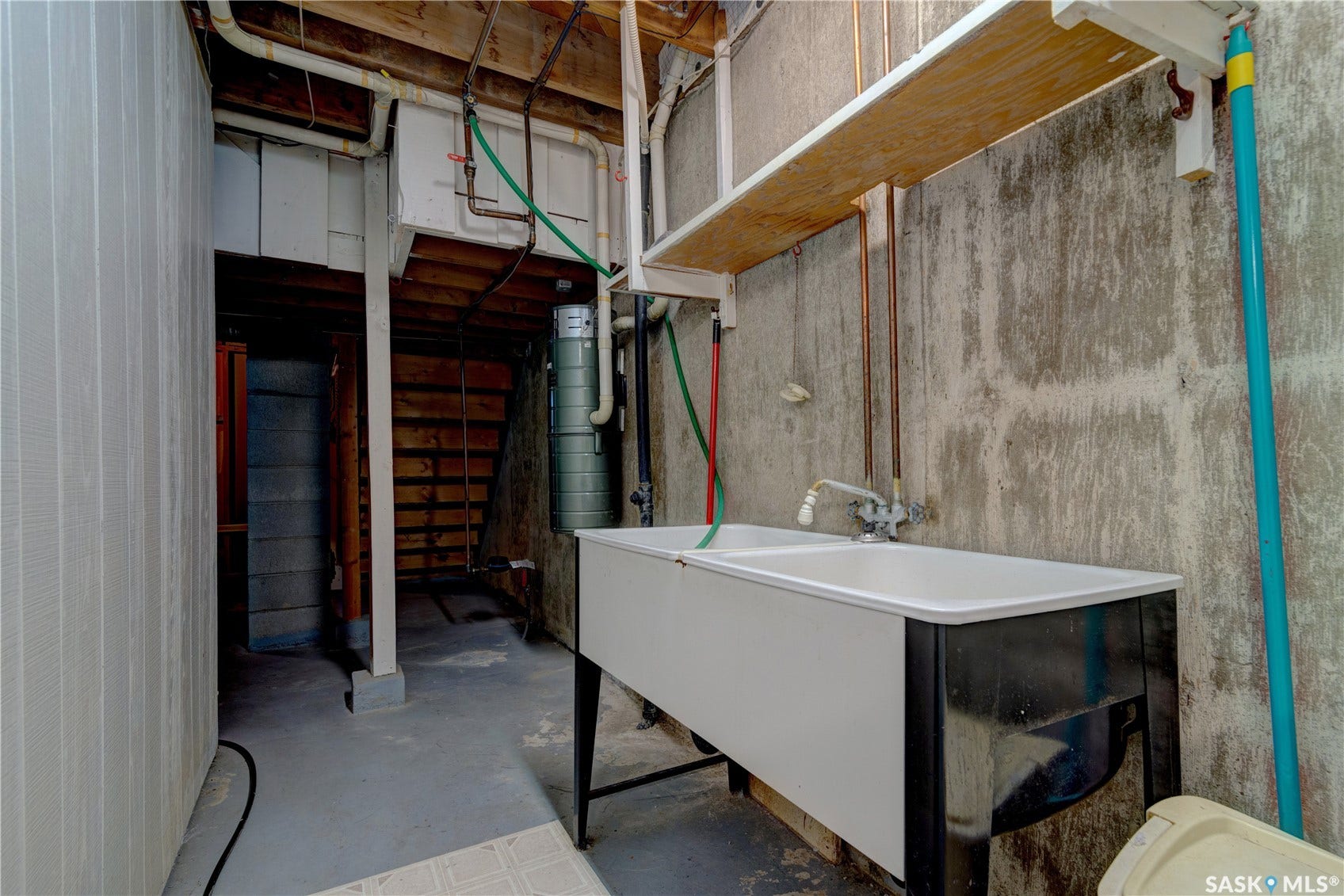 Utility sink with dual basins, exposed concrete walls, and overhead shelving