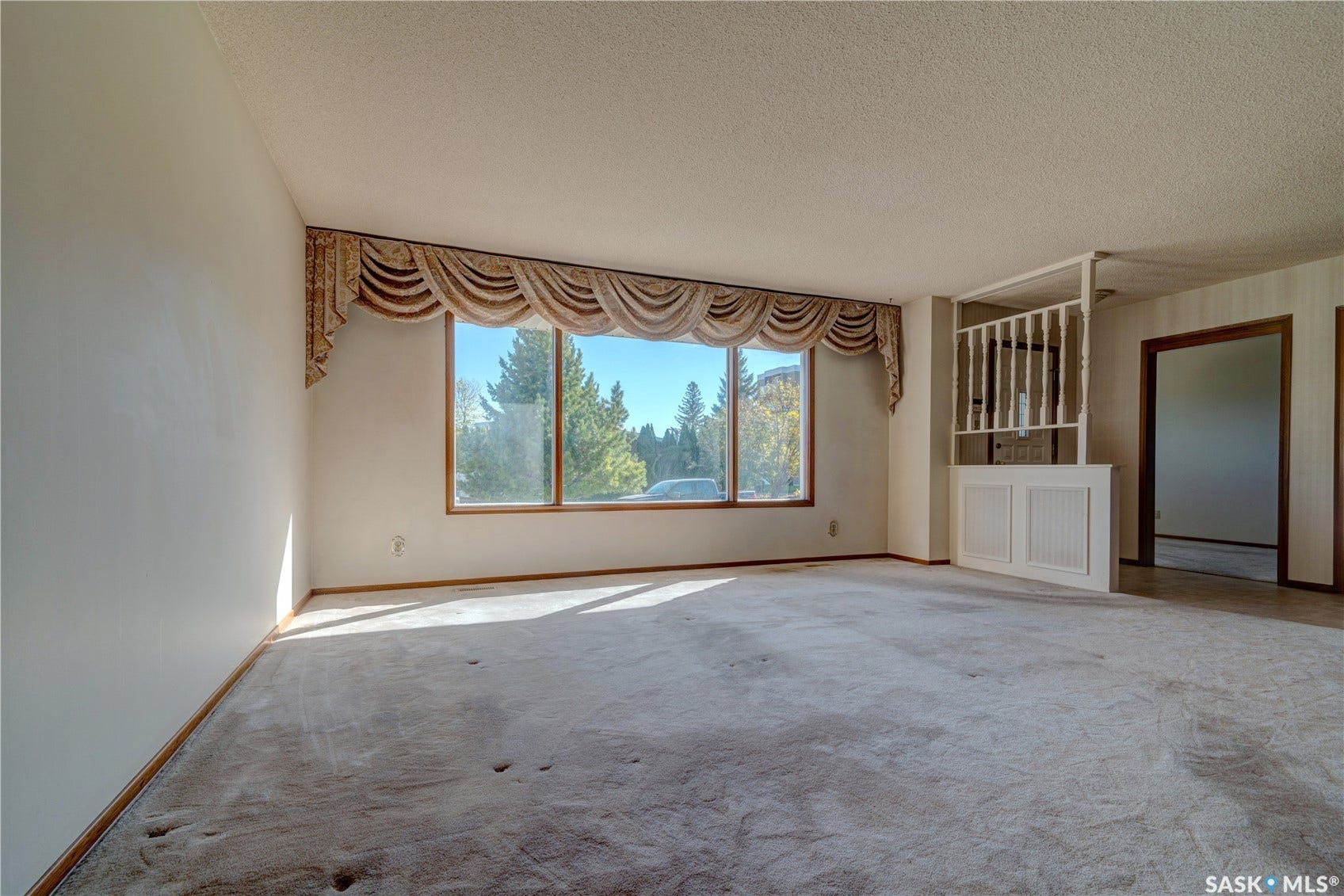 Expansive living area featuring a large window with wood-finish trim, a decorative valance, and a room divider with paneling and spindle details