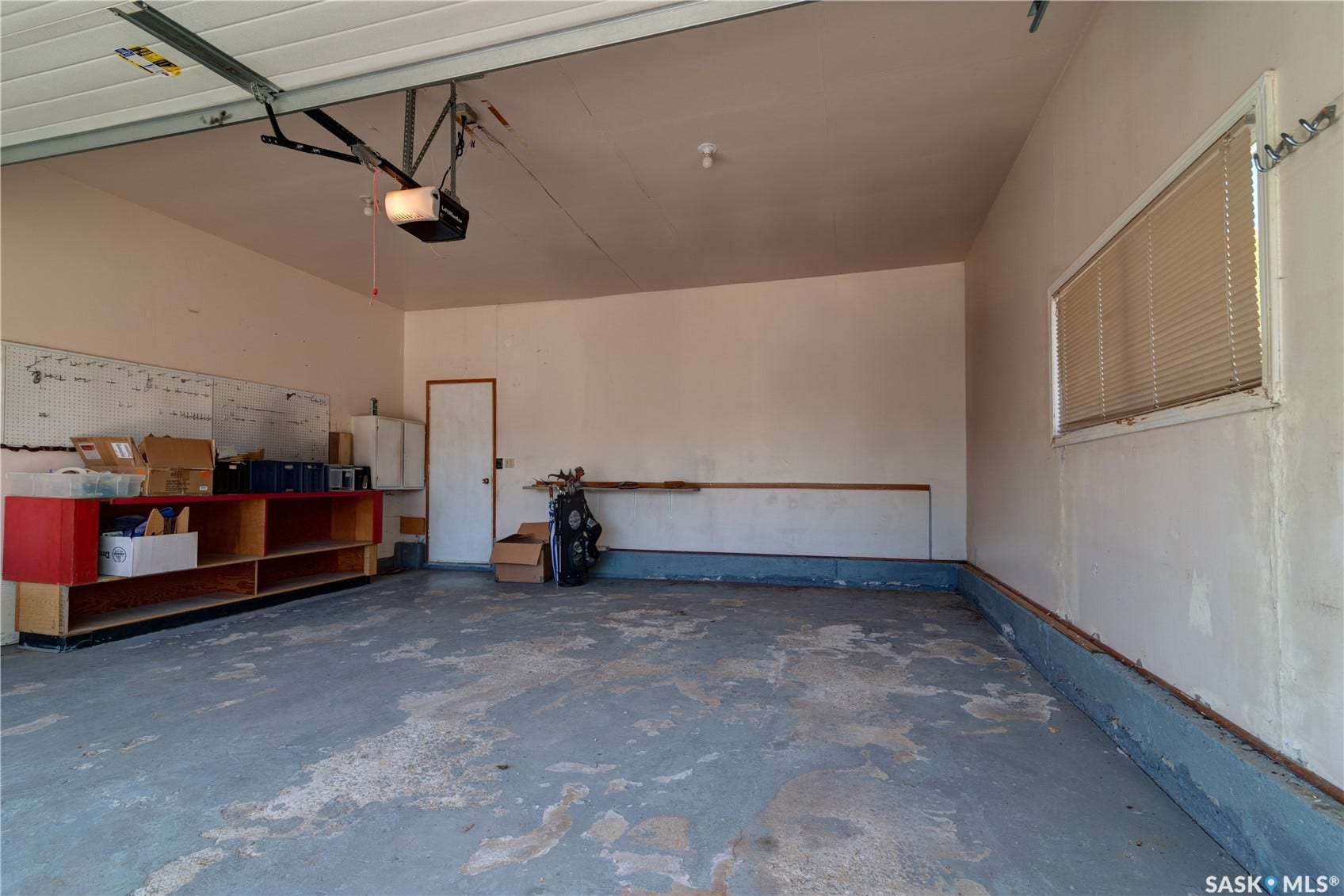 Attached garage with an overhead door opener, concrete flooring, and a large window with blinds