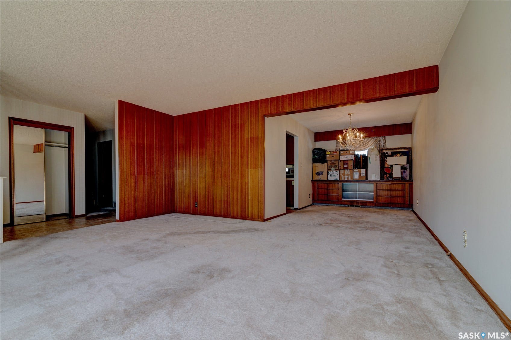 Wall-to-wall carpeting in a neutral tone, wood-paneled accent walls, an overhead chandelier, and built-in cabinetry with glass-front storage