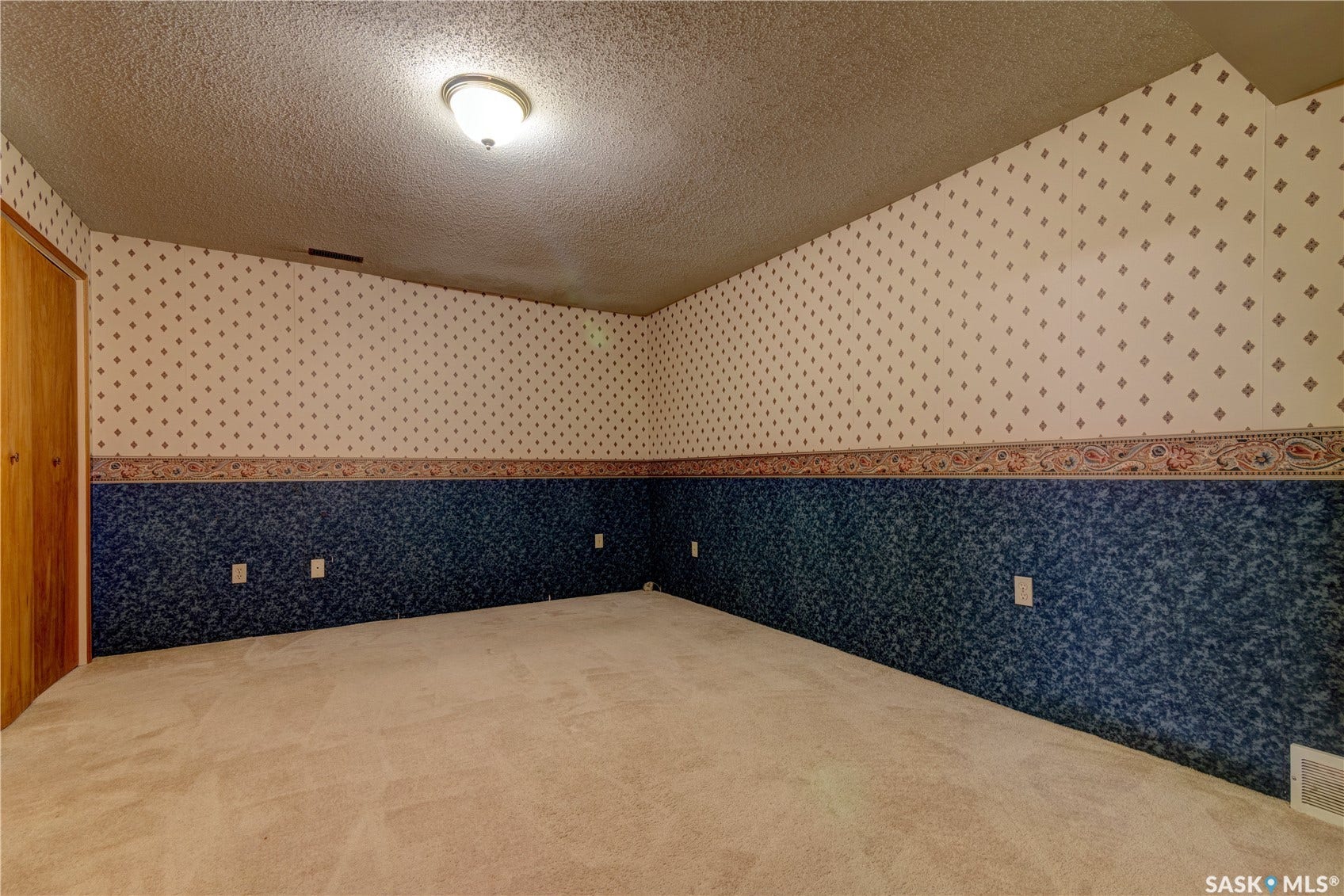 Carpeted flooring, patterned wallpaper, ceiling-mounted light fixture, and wood-finish bifold closet doors