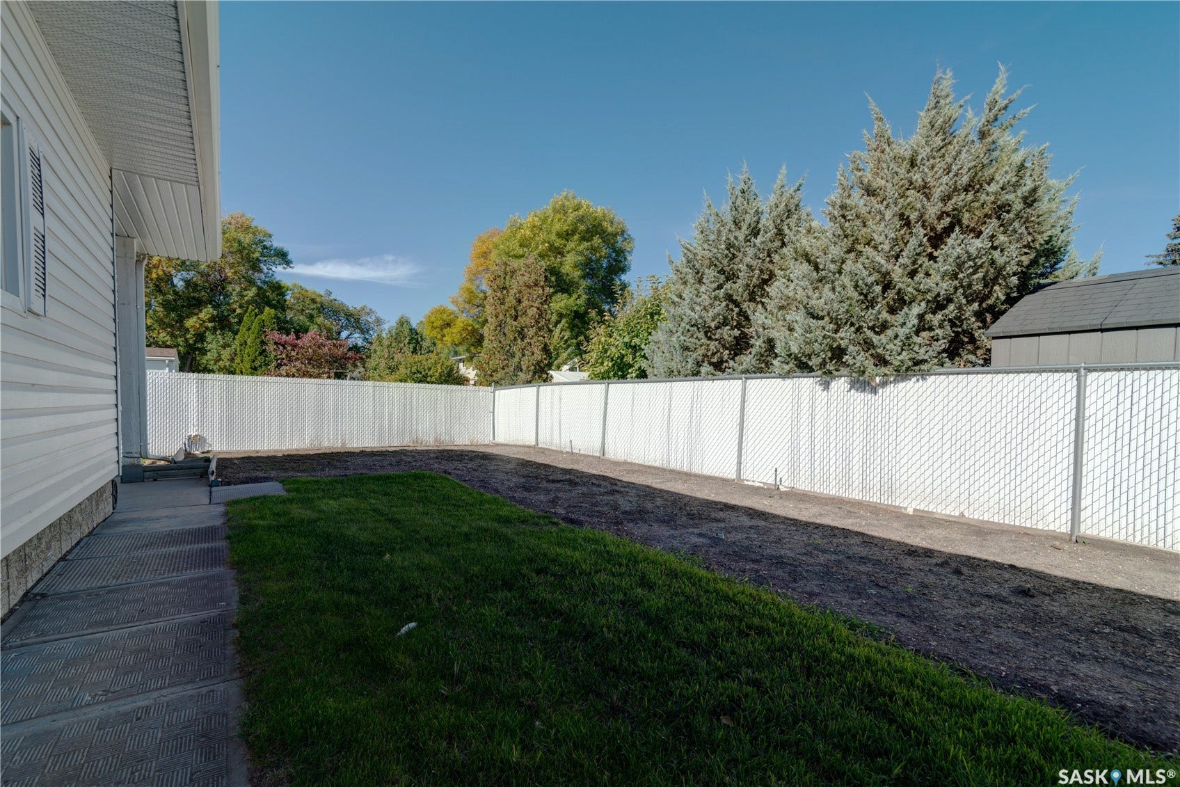 Expansive backyard with a partial lawn, concrete pathway, and full perimeter chain-link fencing with privacy slats