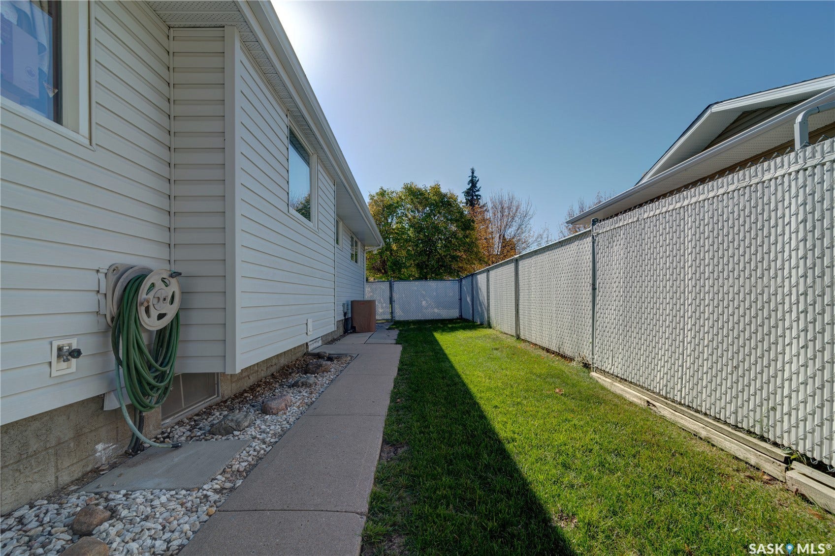 White siding exterior with a concrete walkway, gravel landscaping, a chain-link fence, and a grassy area