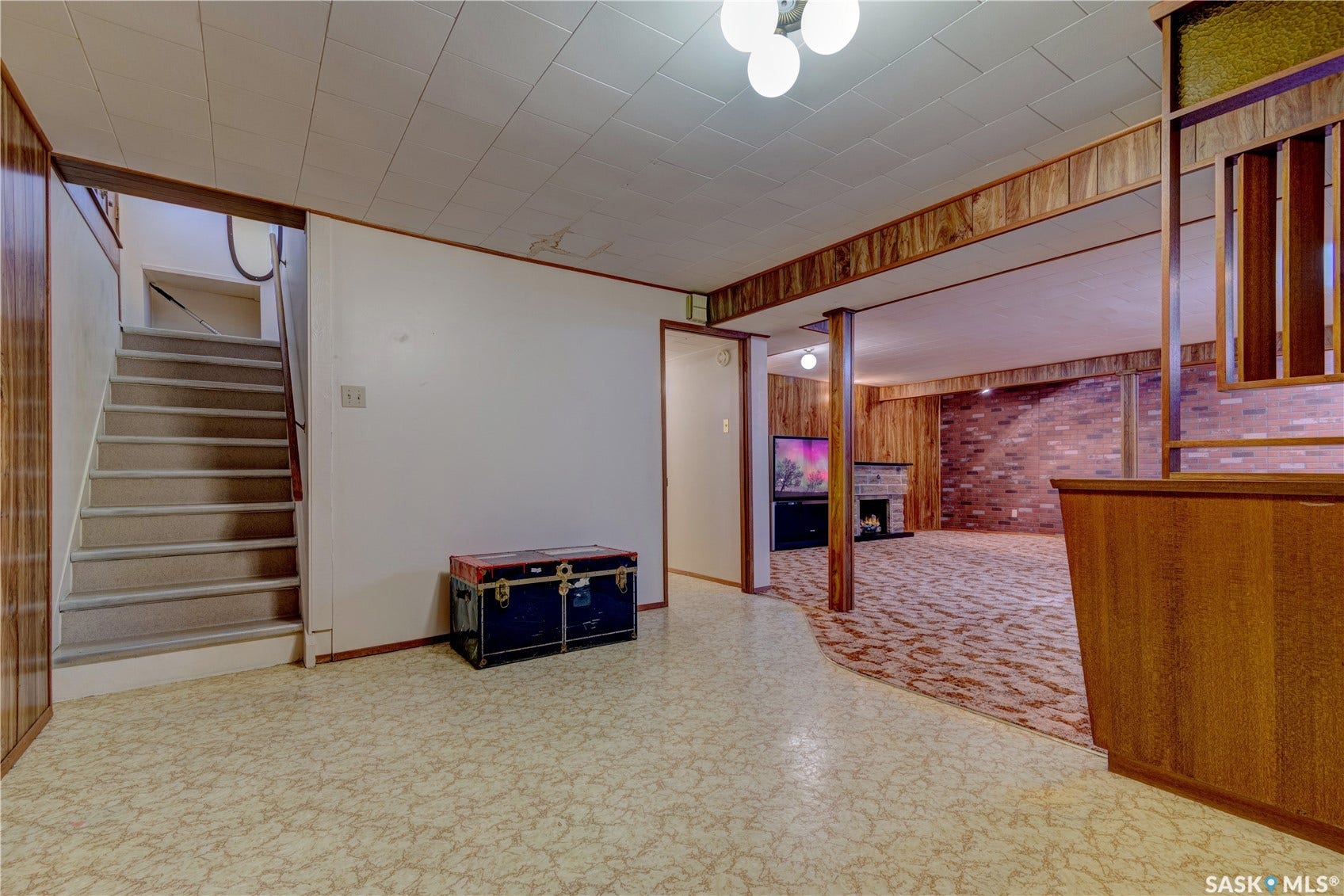 Finished basement area with wood-paneled walls, a built-in bar, and a brick-front fireplace