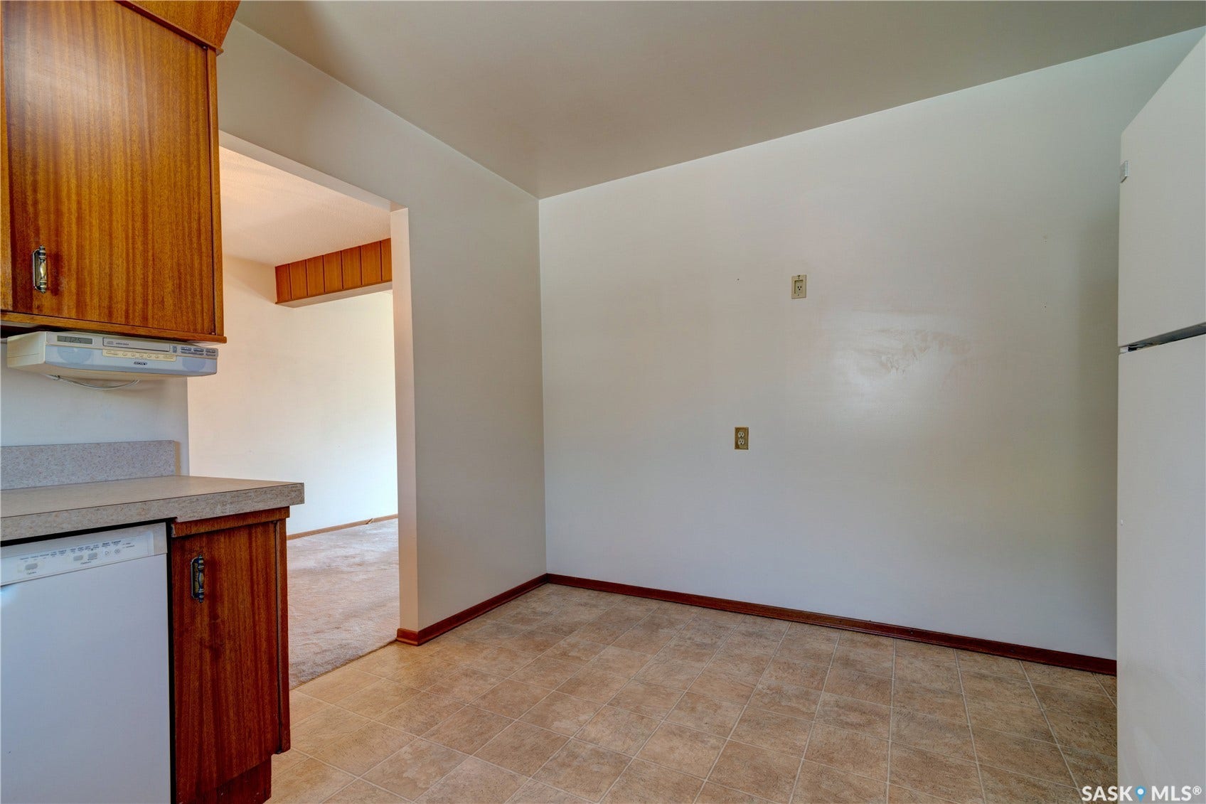 Tile flooring, wood-finish cabinetry, neutral countertop, white dishwasher, and an integrated refrigerator