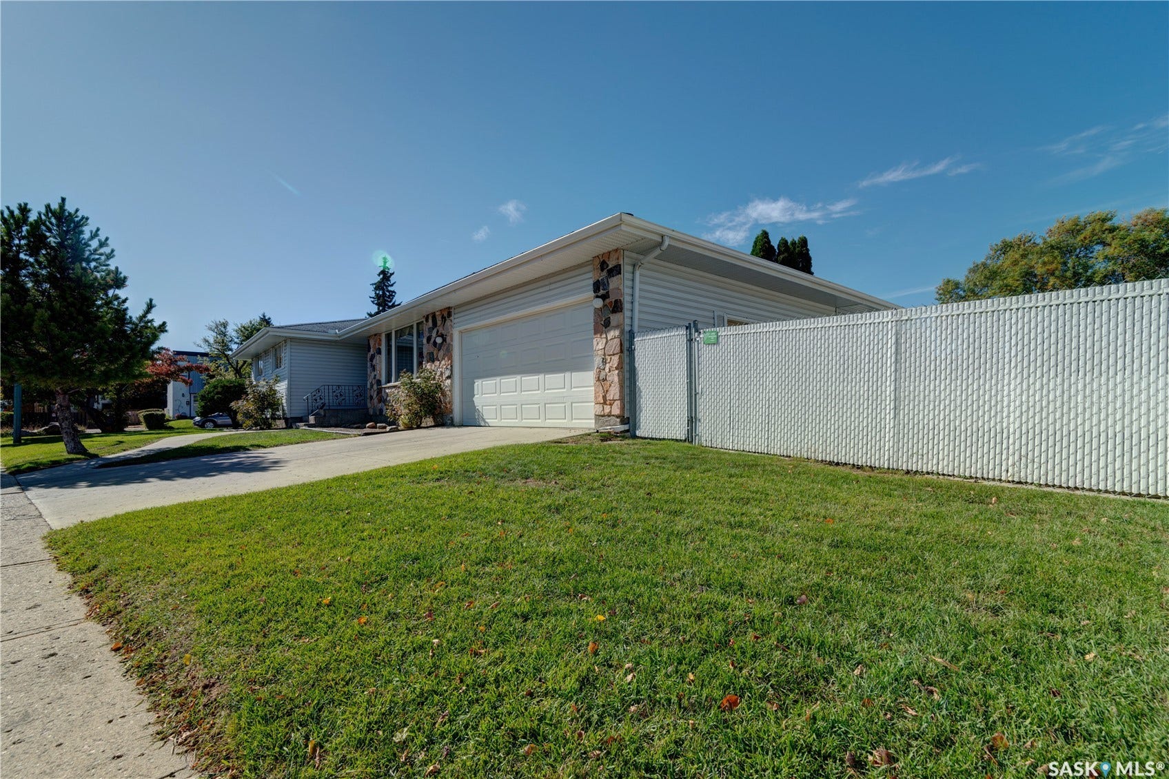 Attached two-car garage, stone and siding exterior, concrete driveway, and chain-link fence