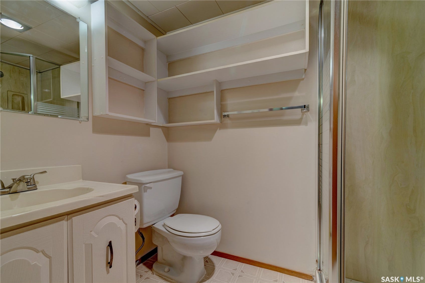 White vanity with a single basin sink, wall-mounted mirror, and overhead lighting