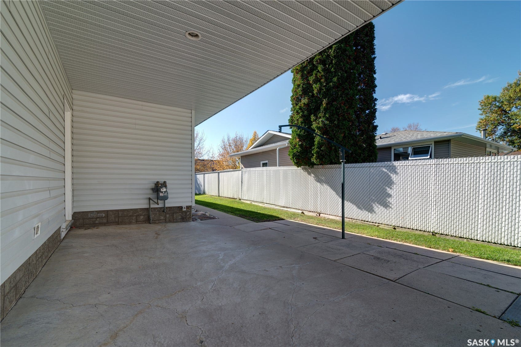 Covered concrete patio with overhead lighting, siding exterior, and a chain-link fence