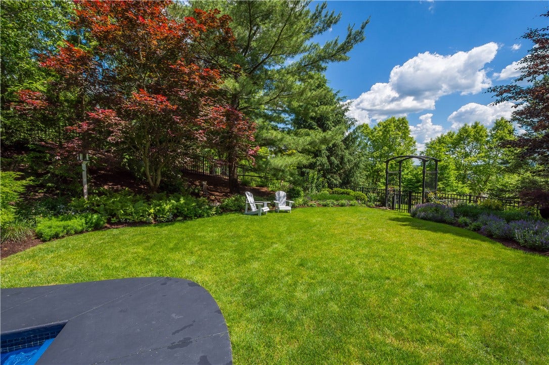 Beyond the pool area, there is plenty of green space surrounded by lush perennial gardens. The yard continues beyond the fenc and arbor.